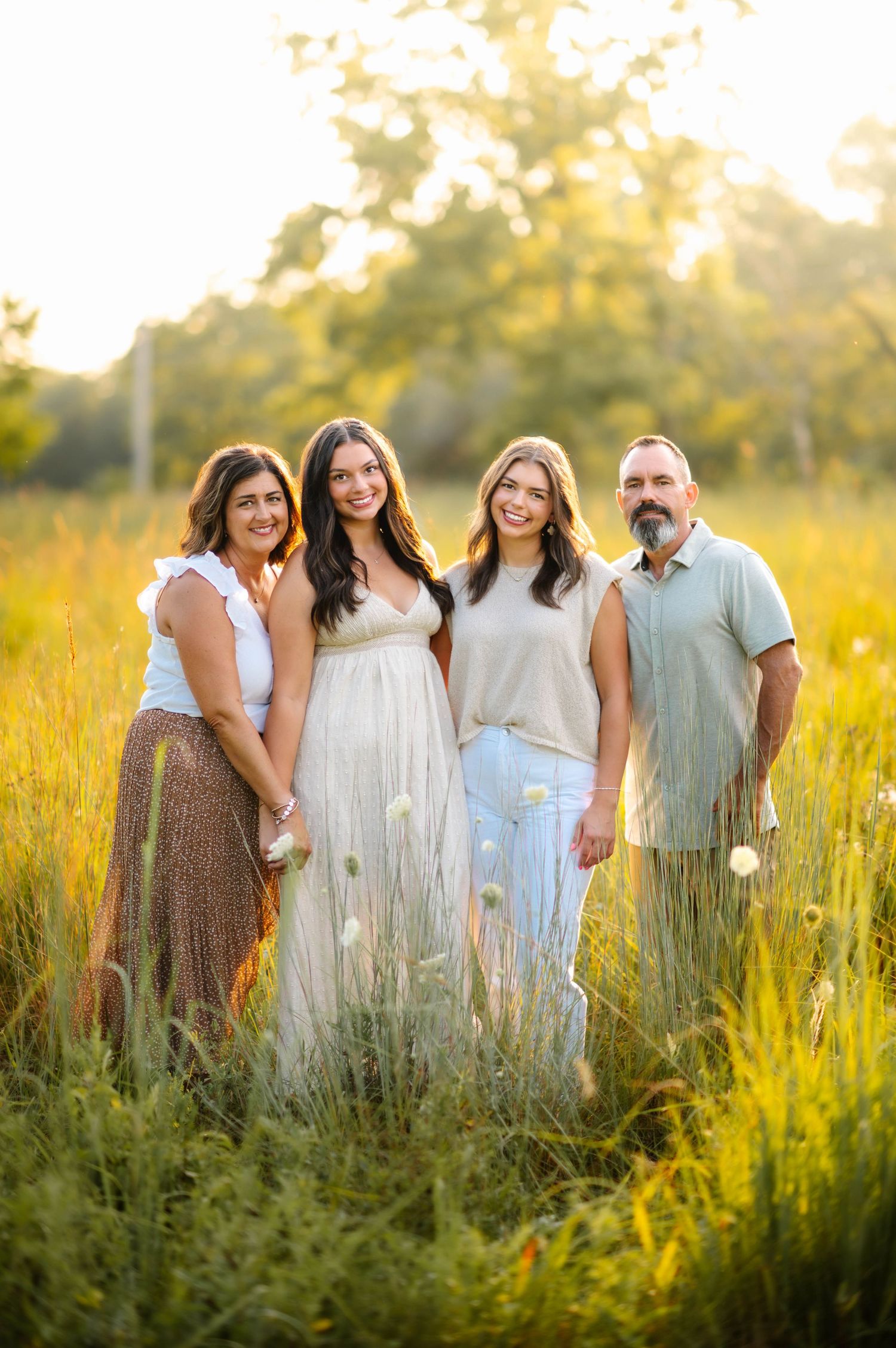 People stand together in coordinated outfits among tall grass during golden hour photography session.