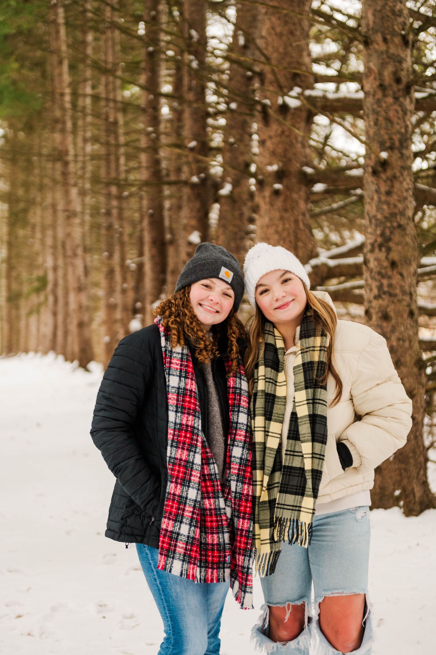 Winter forest photoshoot with people wearing plaid scarves and warm jackets.