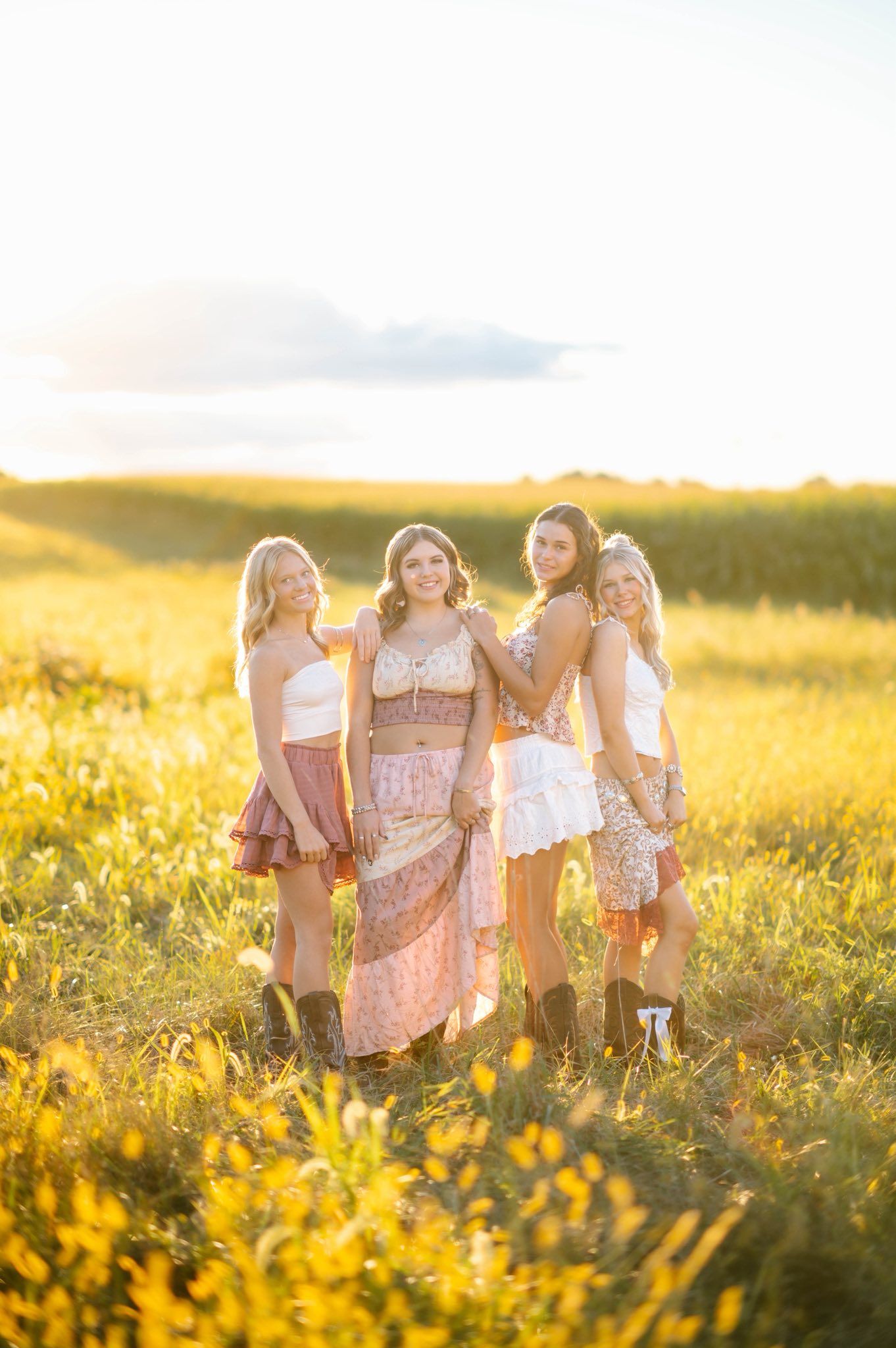 Group gathered in a wildflower meadow wearing light summer dresses during sunset.