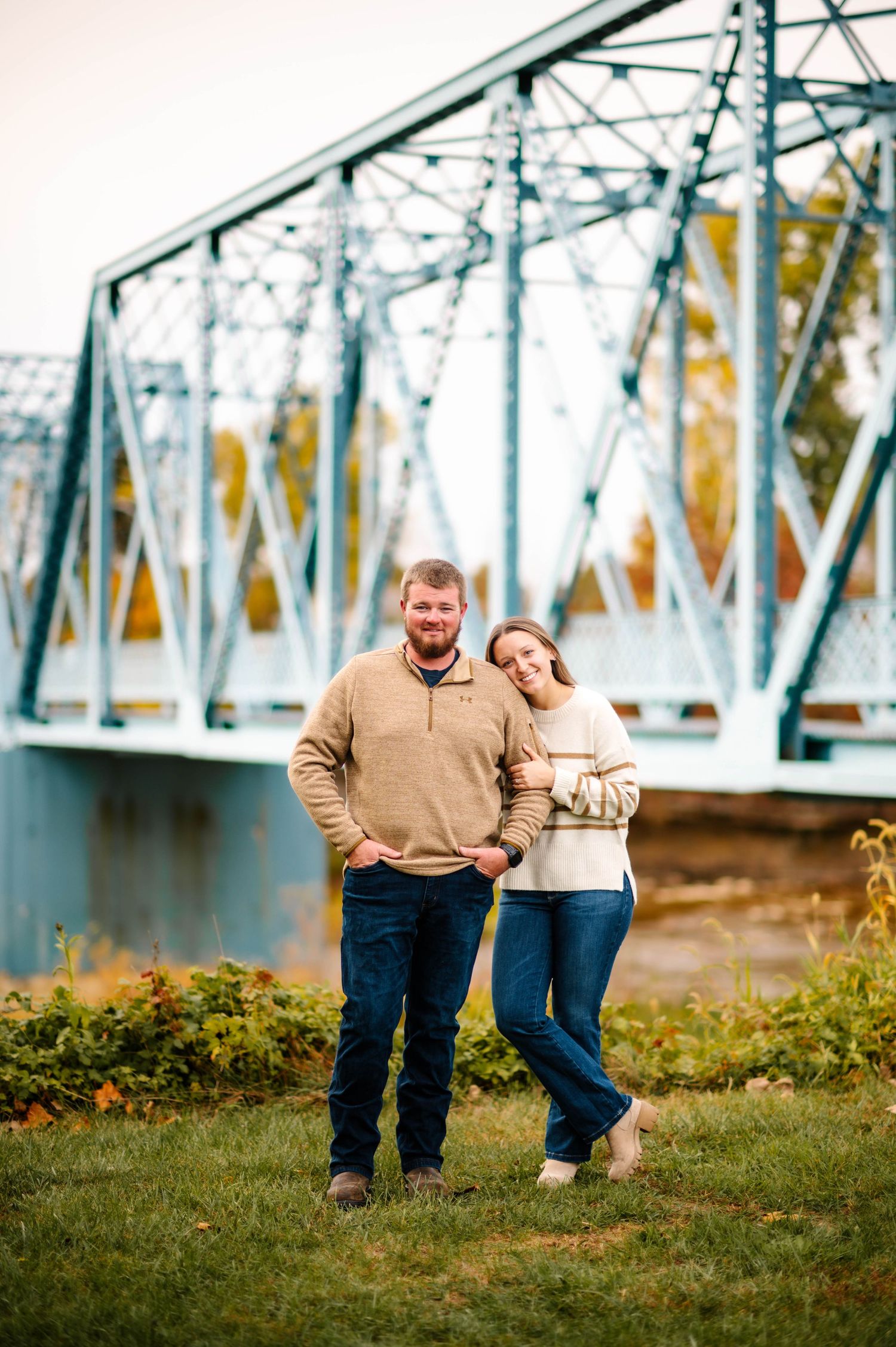 Casual couple poses playfully by historic blue bridge structure.