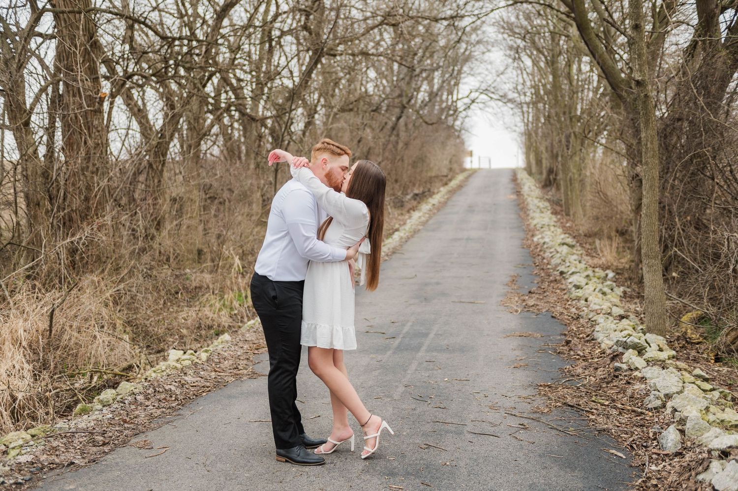 A couple poses for photos on a tree-lined path during winter.