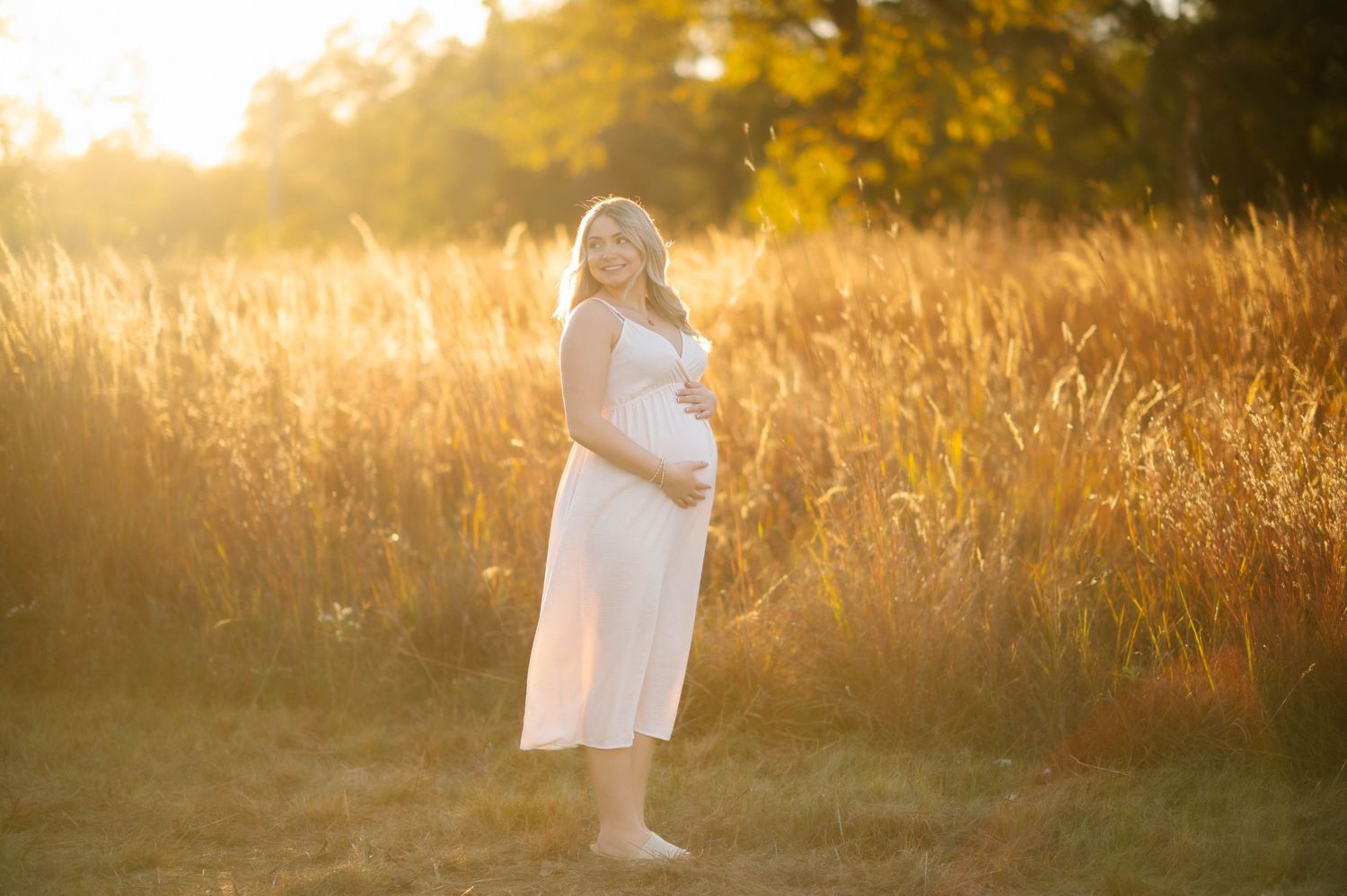 Maternity photoshoot in a golden field at sunset with warm glowing light.