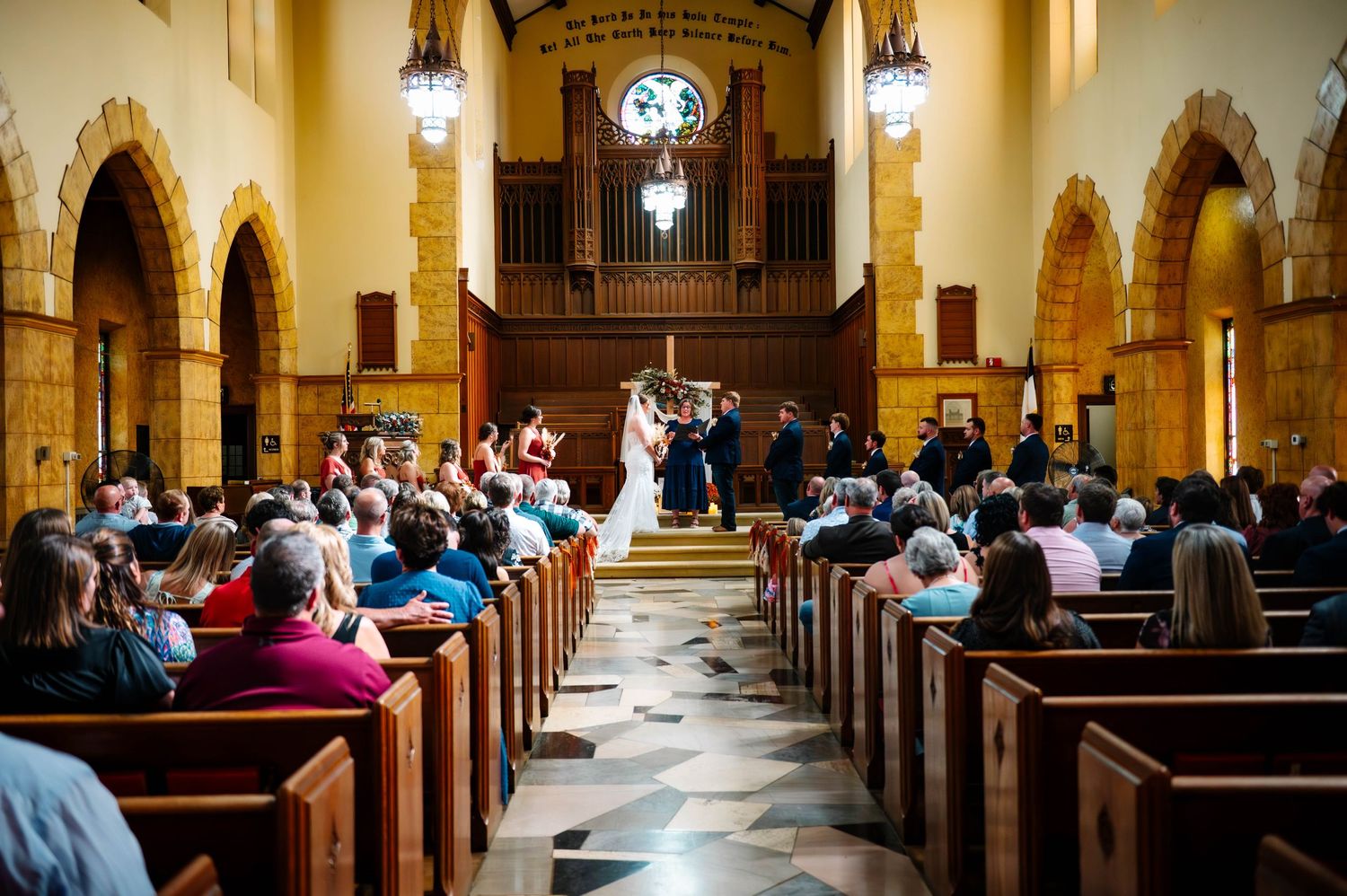 Panoramic view of a church interior during a wedding ceremony with vaulted ceilings and stone columns.