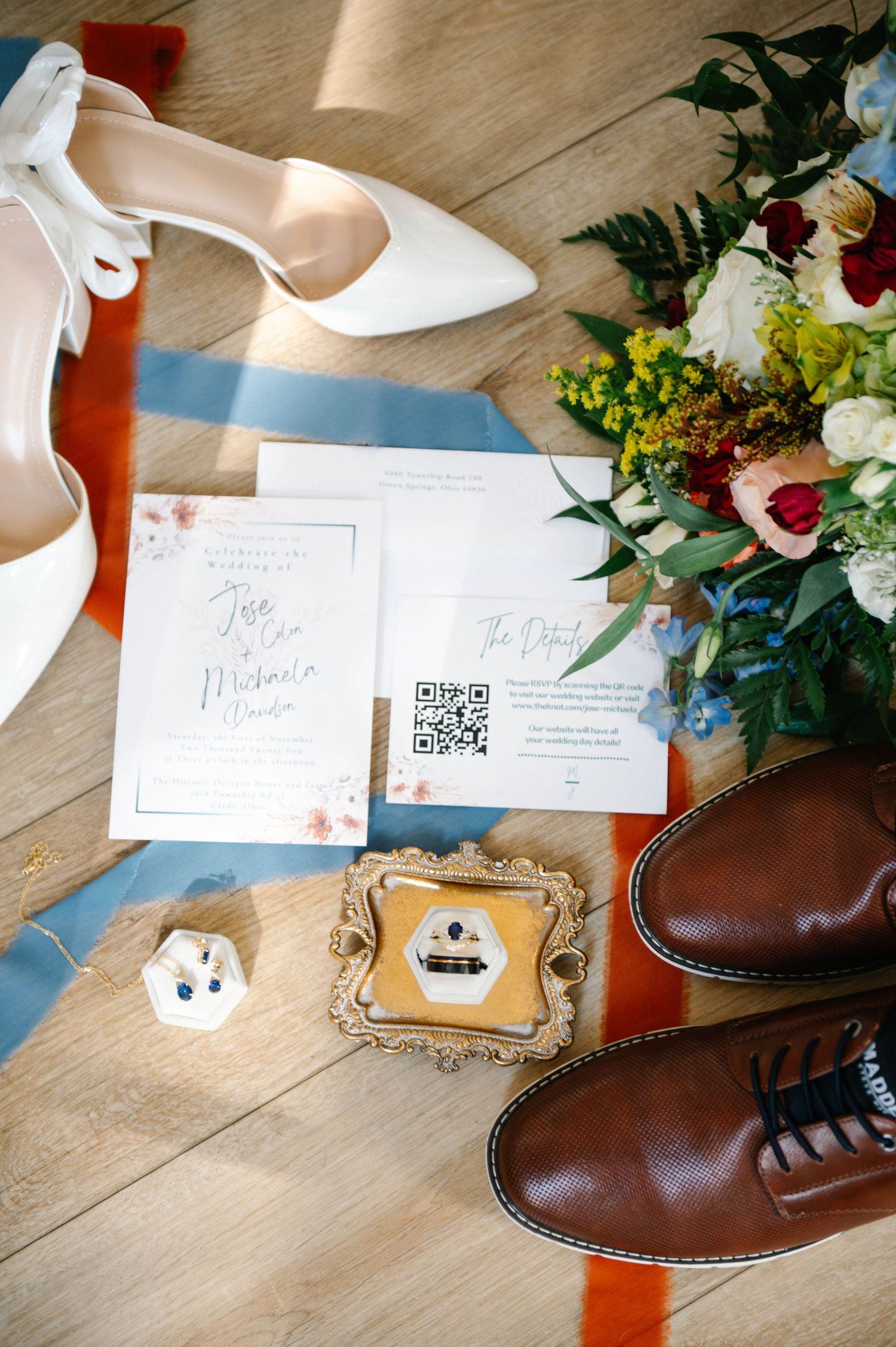 Wedding details with brown leather shoes and floral invitations on wooden floor.