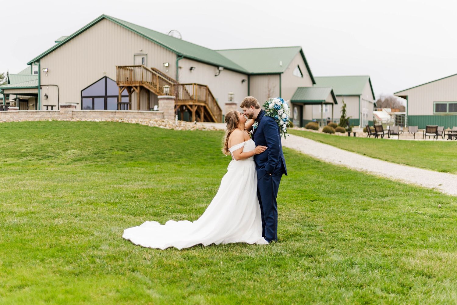 A couple poses together on their wedding day outside a rustic venue with green roofing.