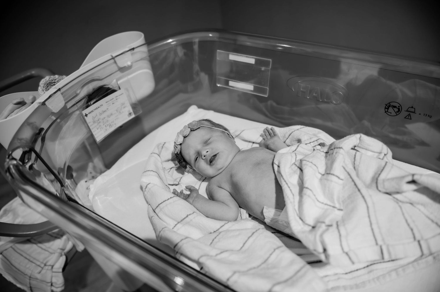 A newborn baby sleeps in a hospital bassinet surrounded by medical monitoring devices.