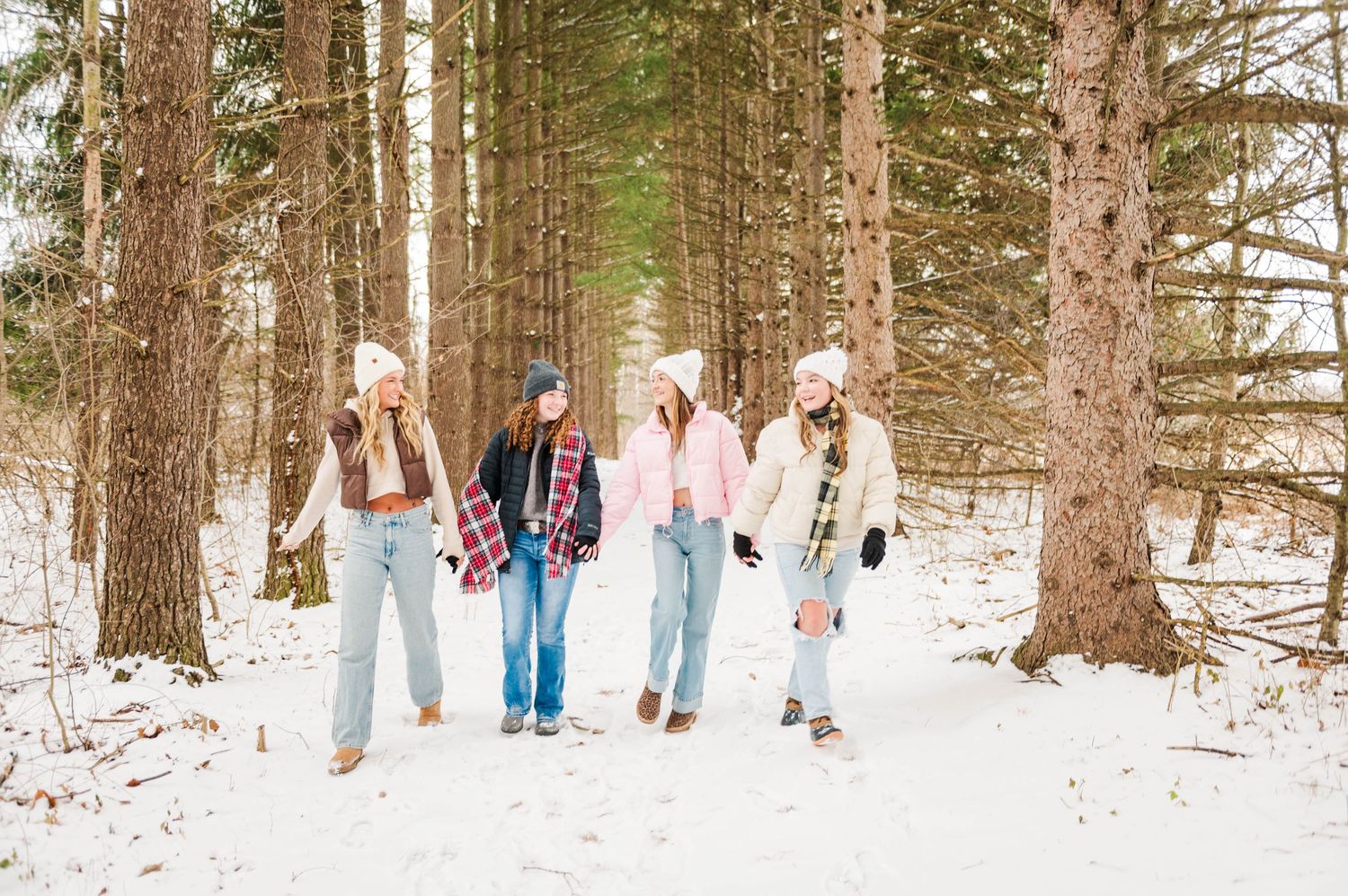 Friends walking through snowy forest path wearing winter attire and denim.
