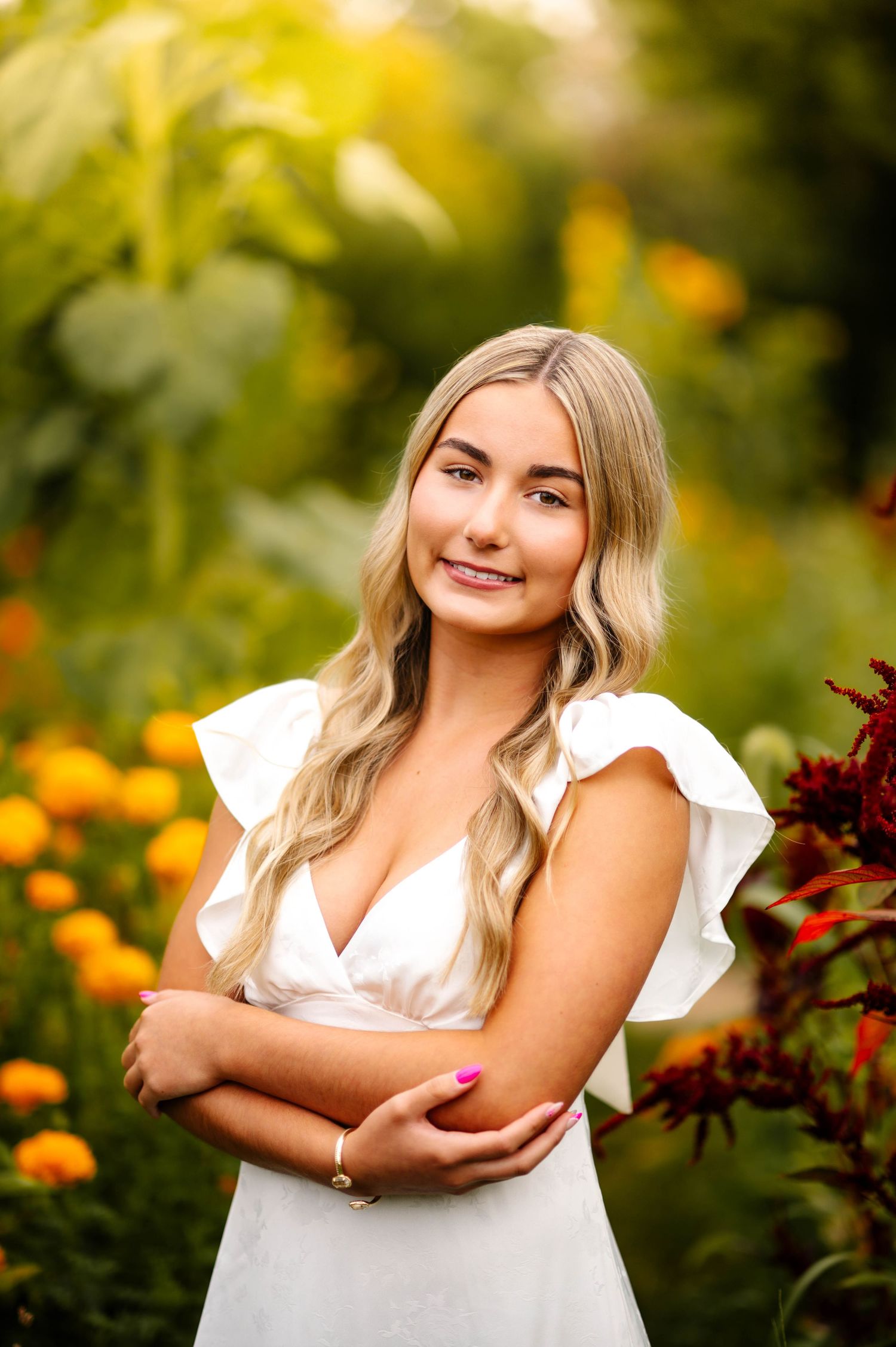 Senior portrait in a white dress surrounded by colorful flowers and greenery.