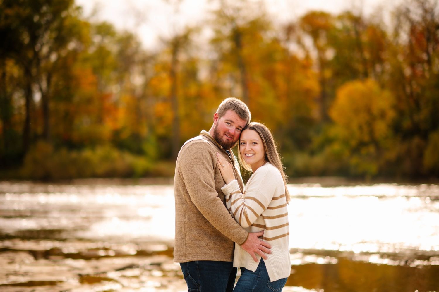 Romantic couple shares intimate moment on rocky shore during sunset with fall colors.