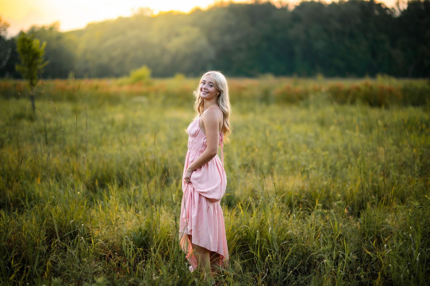 A pink dress flows in a golden field at sunset creating a dreamy summer scene.
