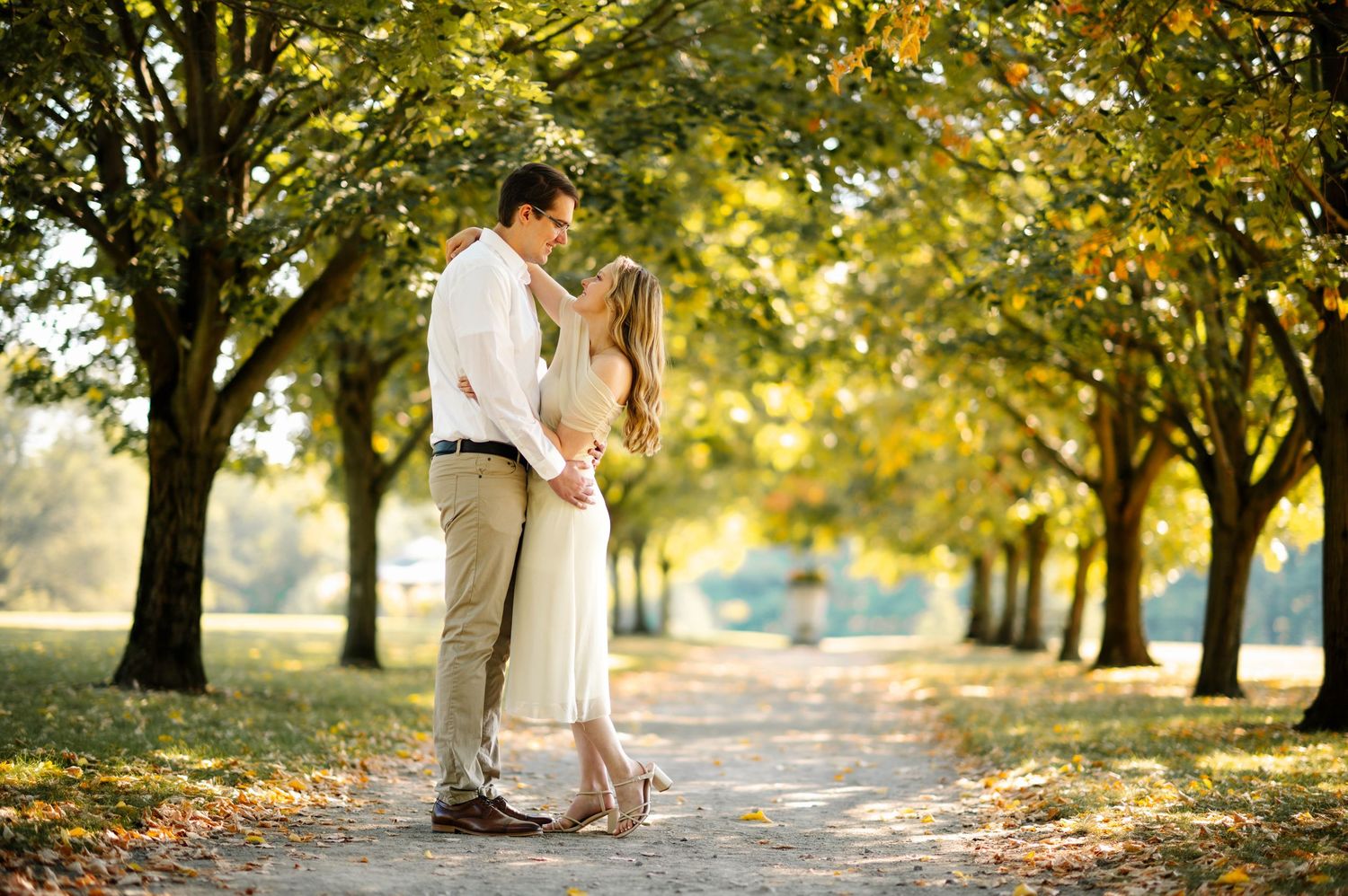 Romantic couple poses along a tree-lined path during golden hour sunset for wedding photos.