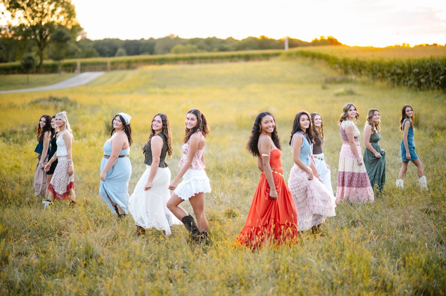 People in colorful dresses gather for photos in a sunlit field.