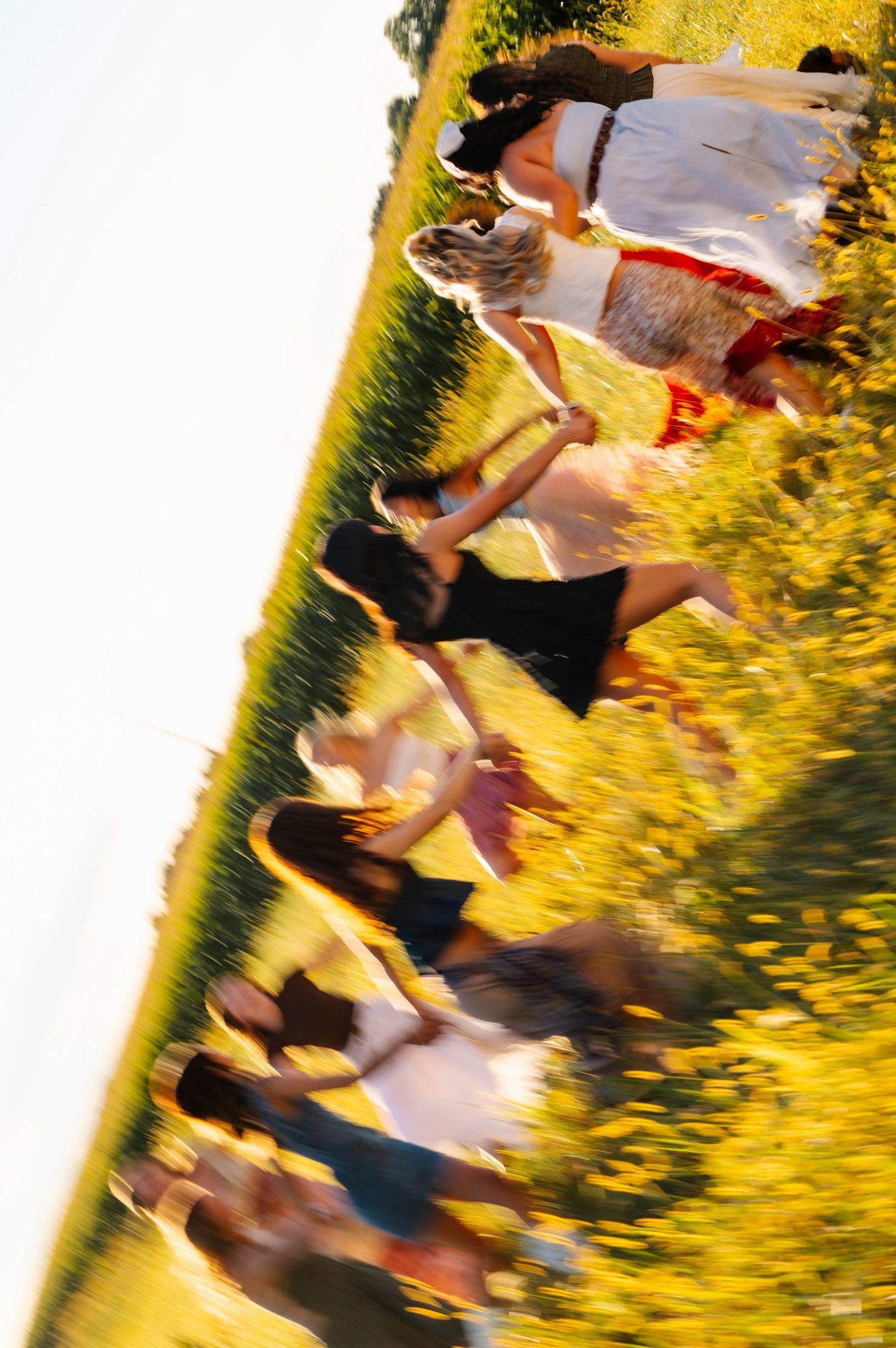 Motion-blurred shot of people dancing in a field during sunset creating an artistic effect.