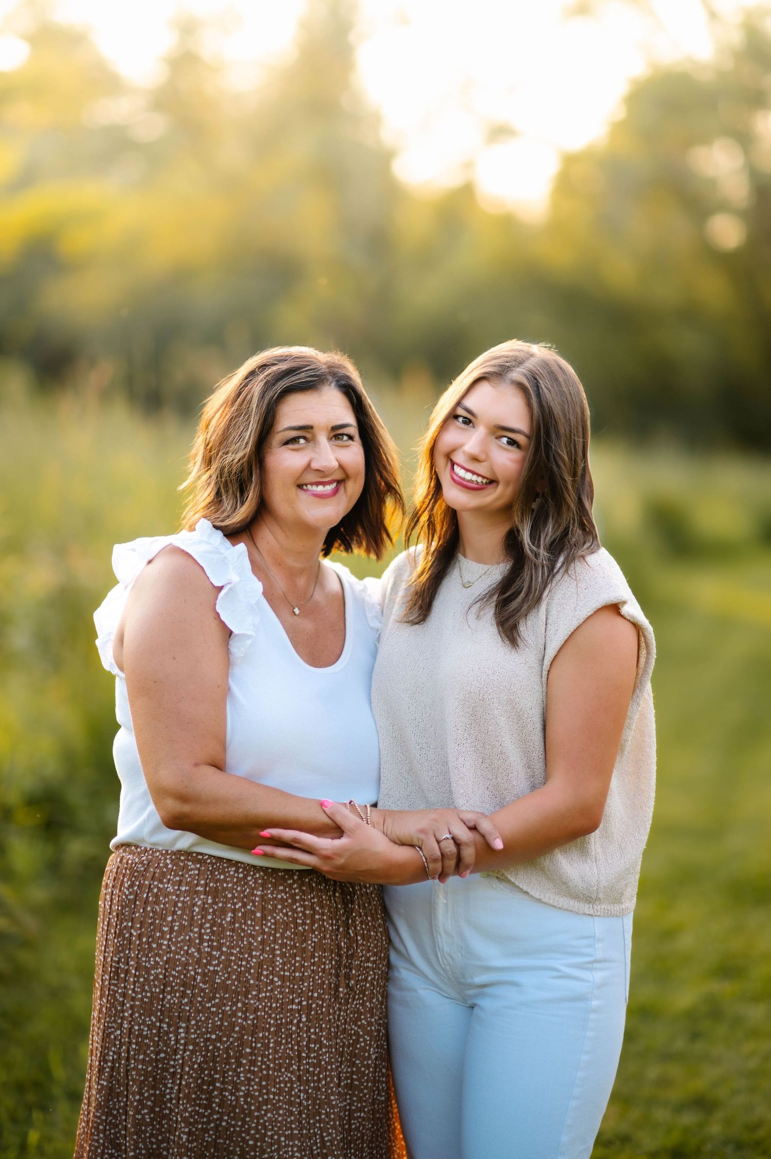 Two people share a warm embrace while posing in a sunlit field.