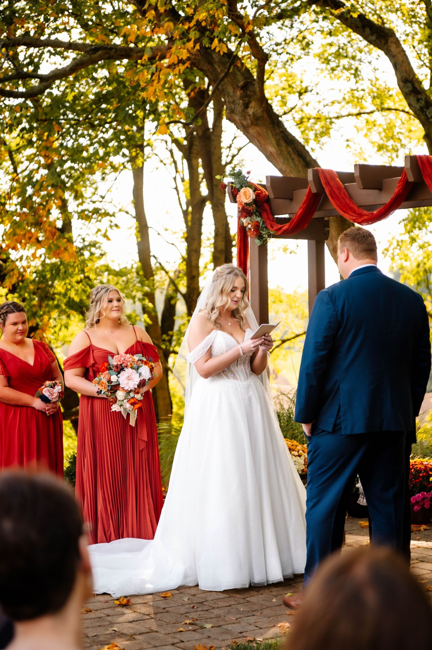 Wedding ceremony setup with red bridesmaid dresses against autumn foliage.
