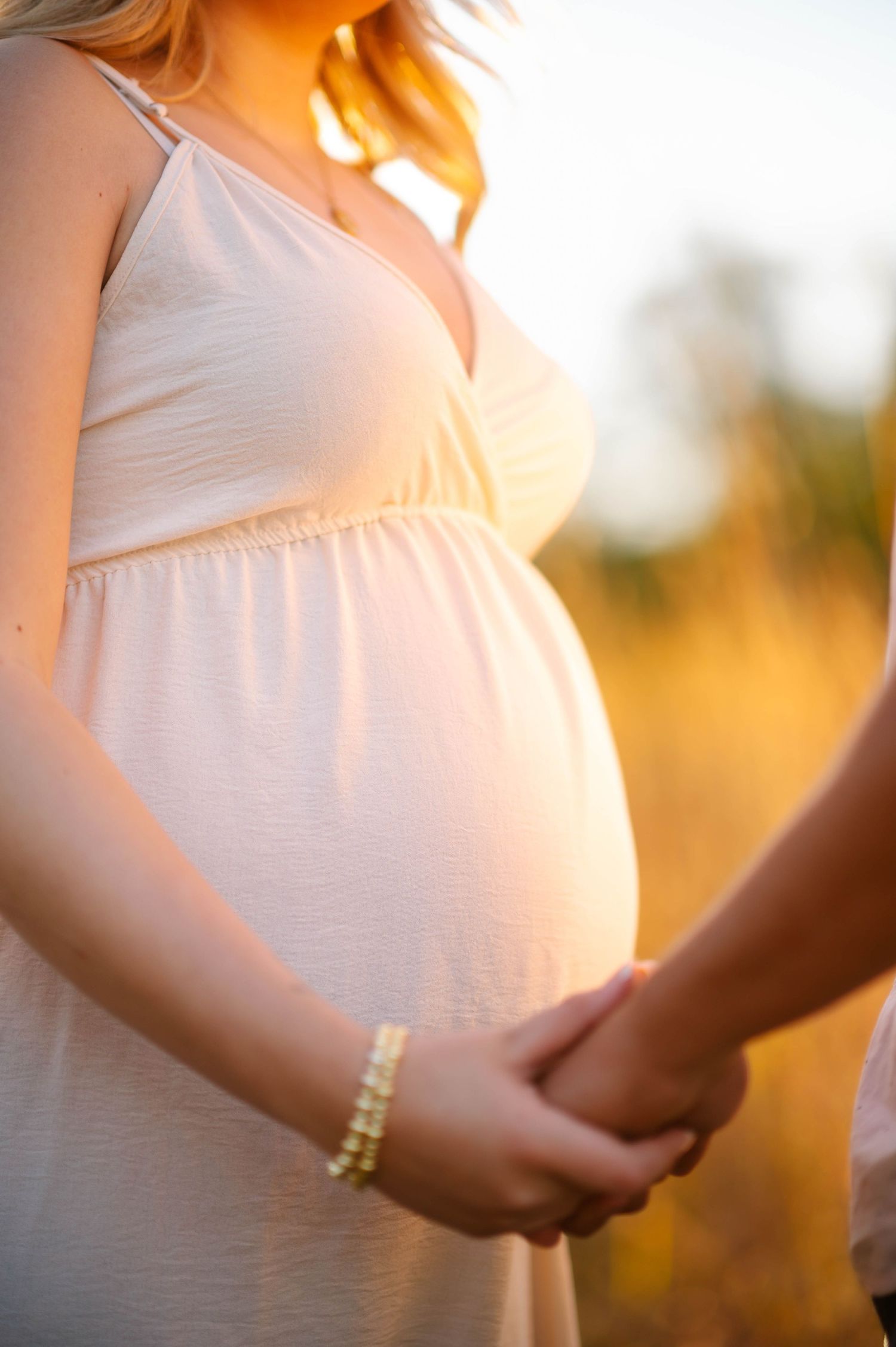 Close up of pregnant belly in white dress with sunlight creating a warm glow.