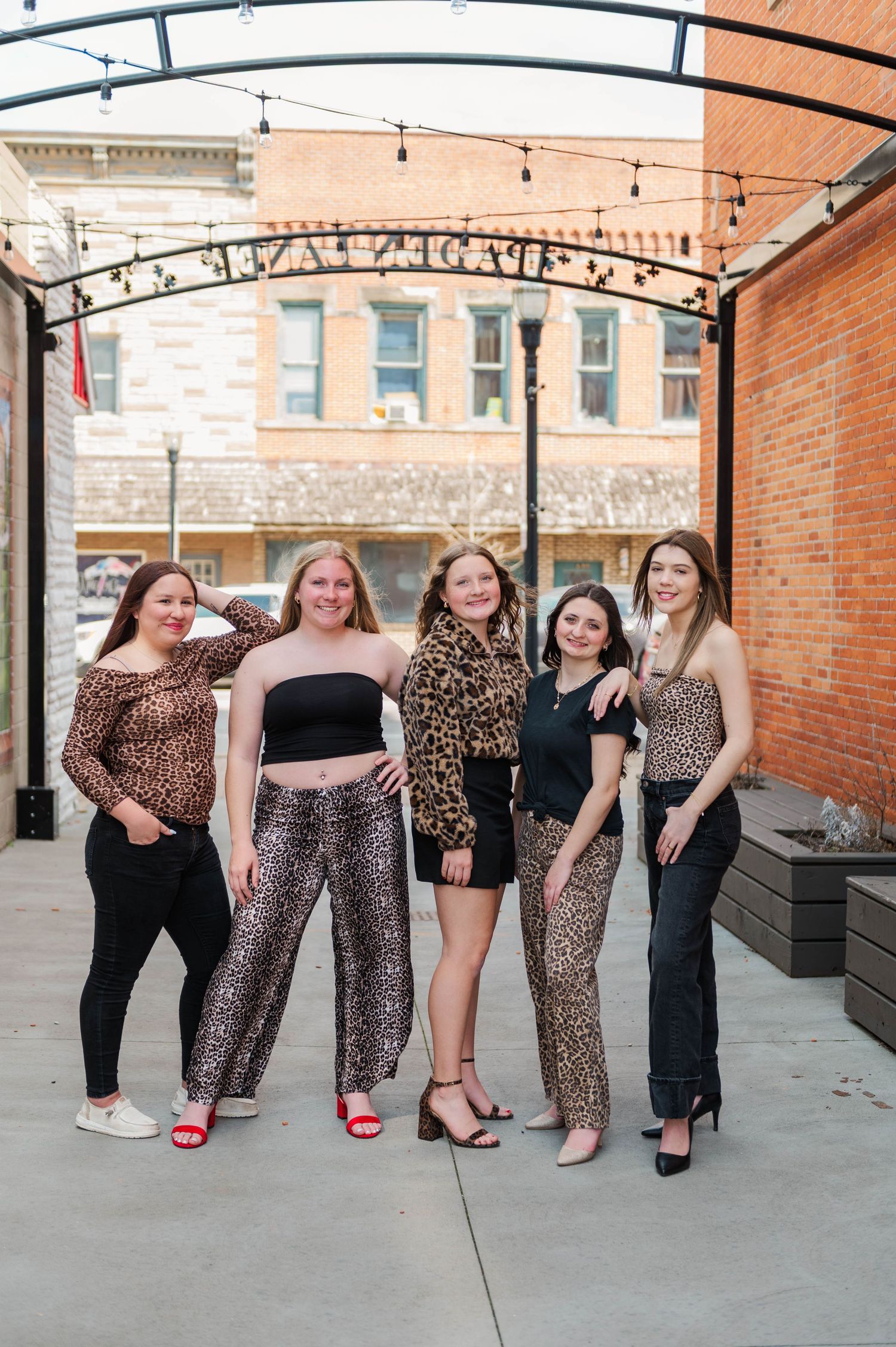 Five young women wearing coordinating leopard print outfits smile and pose under string lights outdoors.