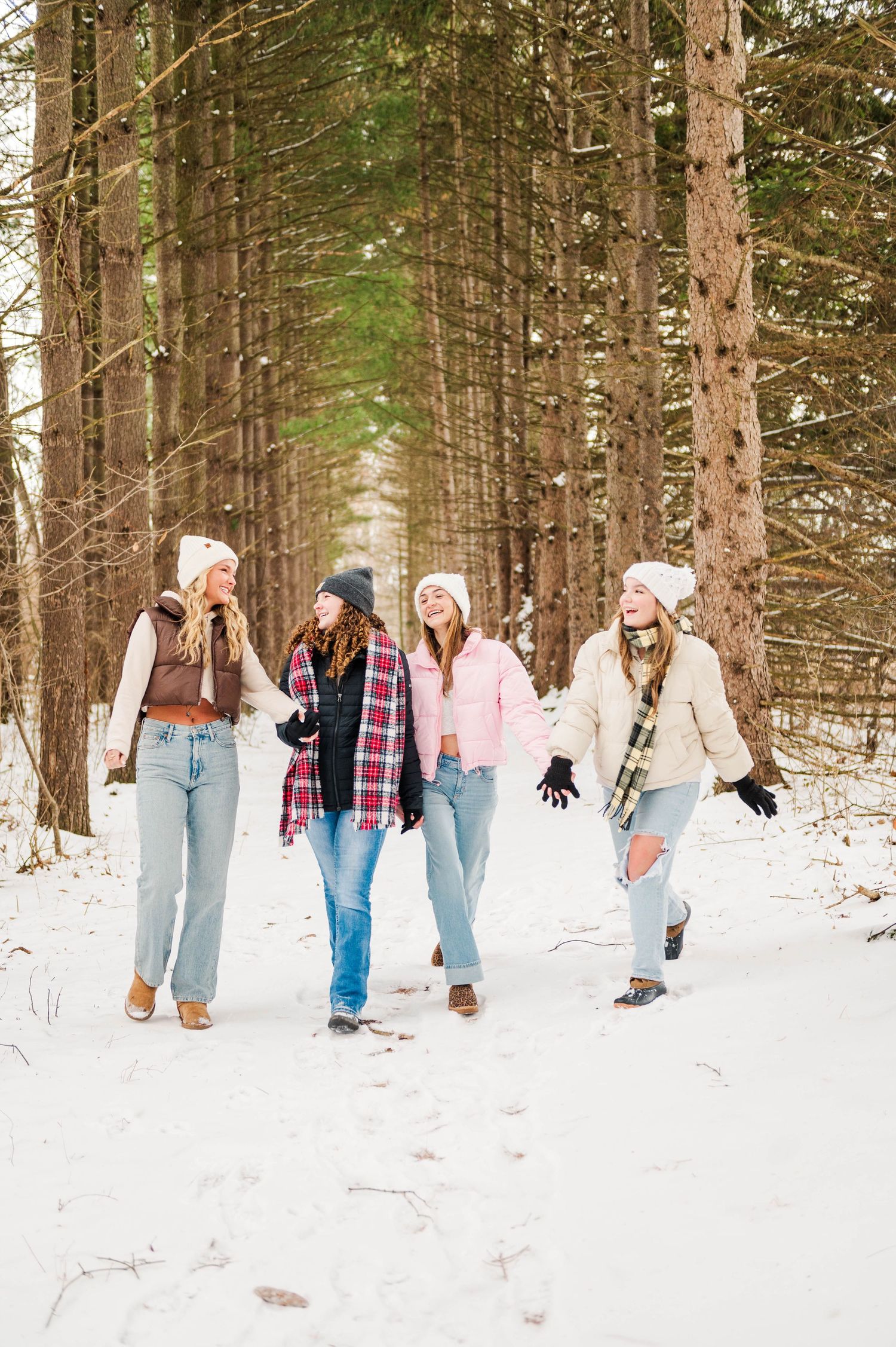 Group walking through snowy forest path wearing winter clothing.