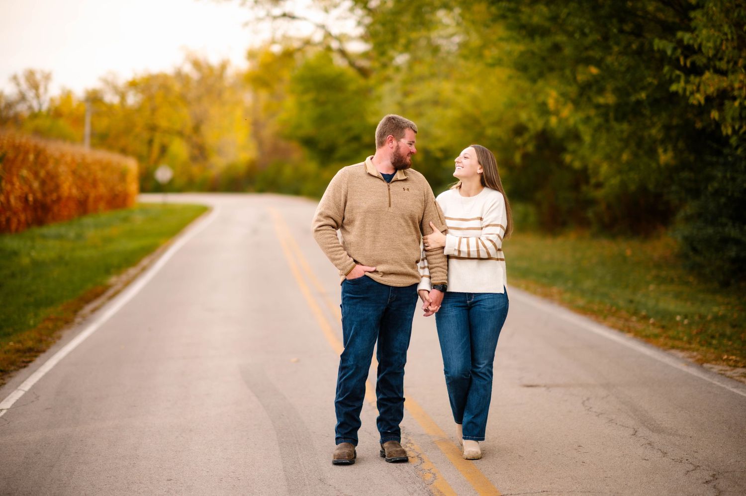 Two people walk together on an autumn road surrounded by fall foliage.