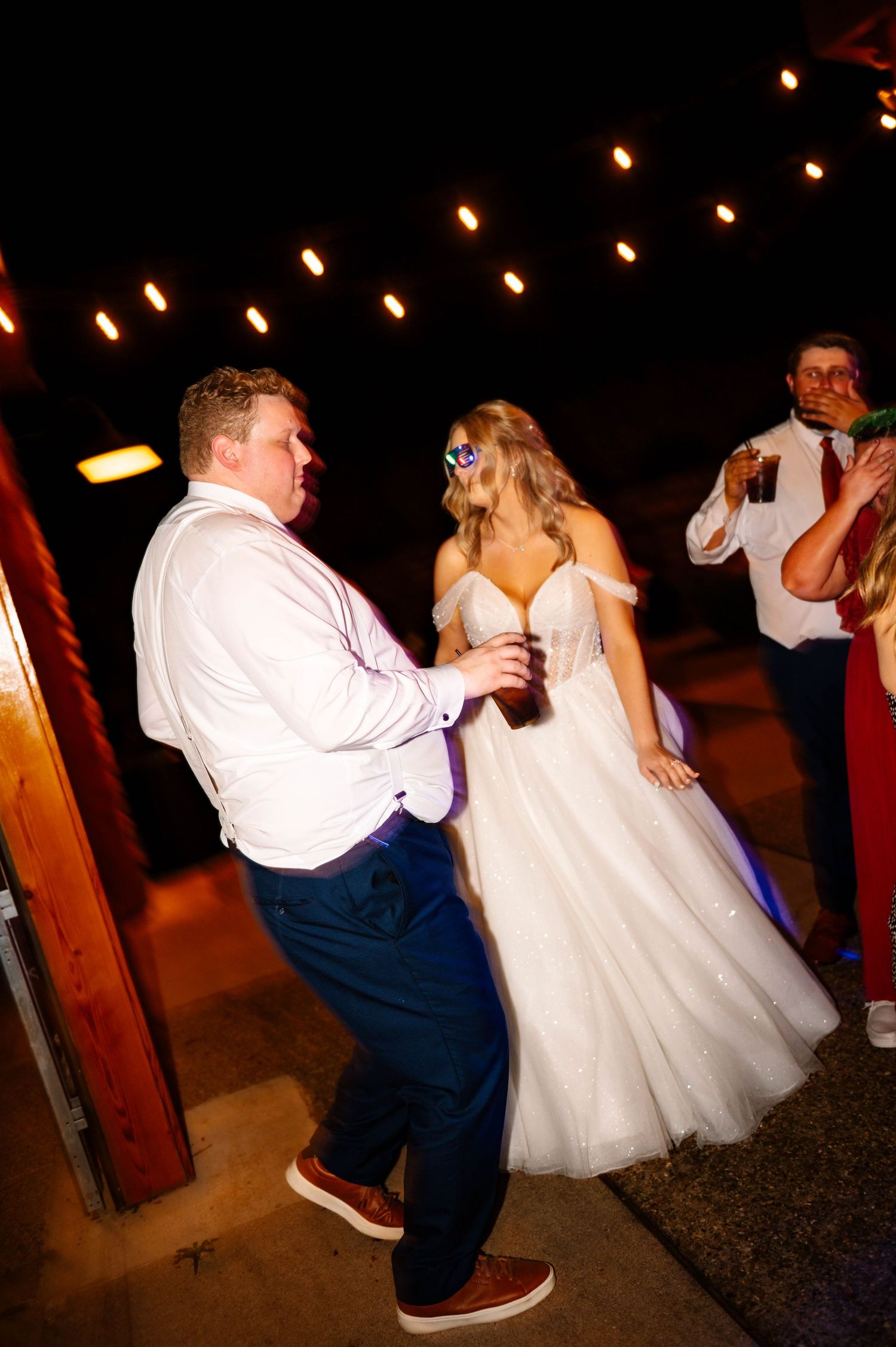 Dancing couple illuminated by string lights during an evening wedding reception.