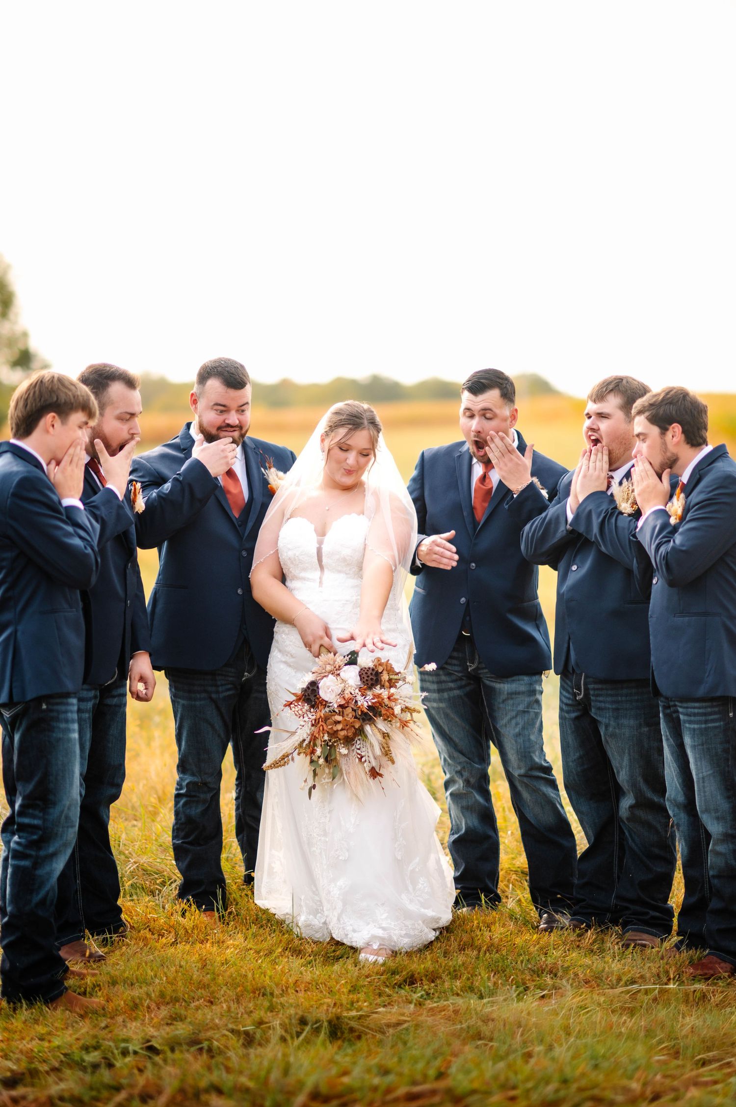 Wedding party laughing together in a line across golden field at sunset.