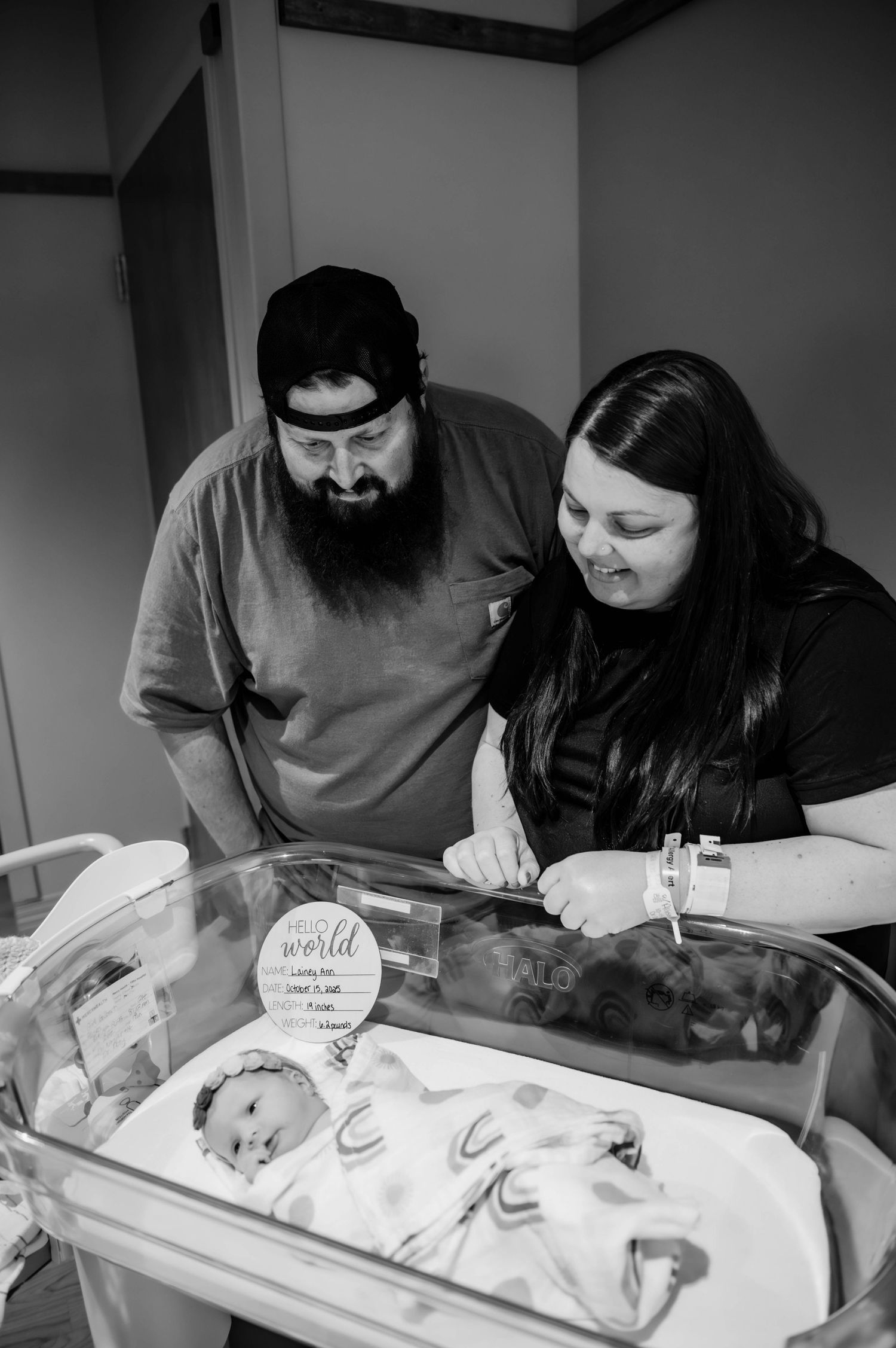 Caregivers looking down at a newborn baby in a hospital bassinet.