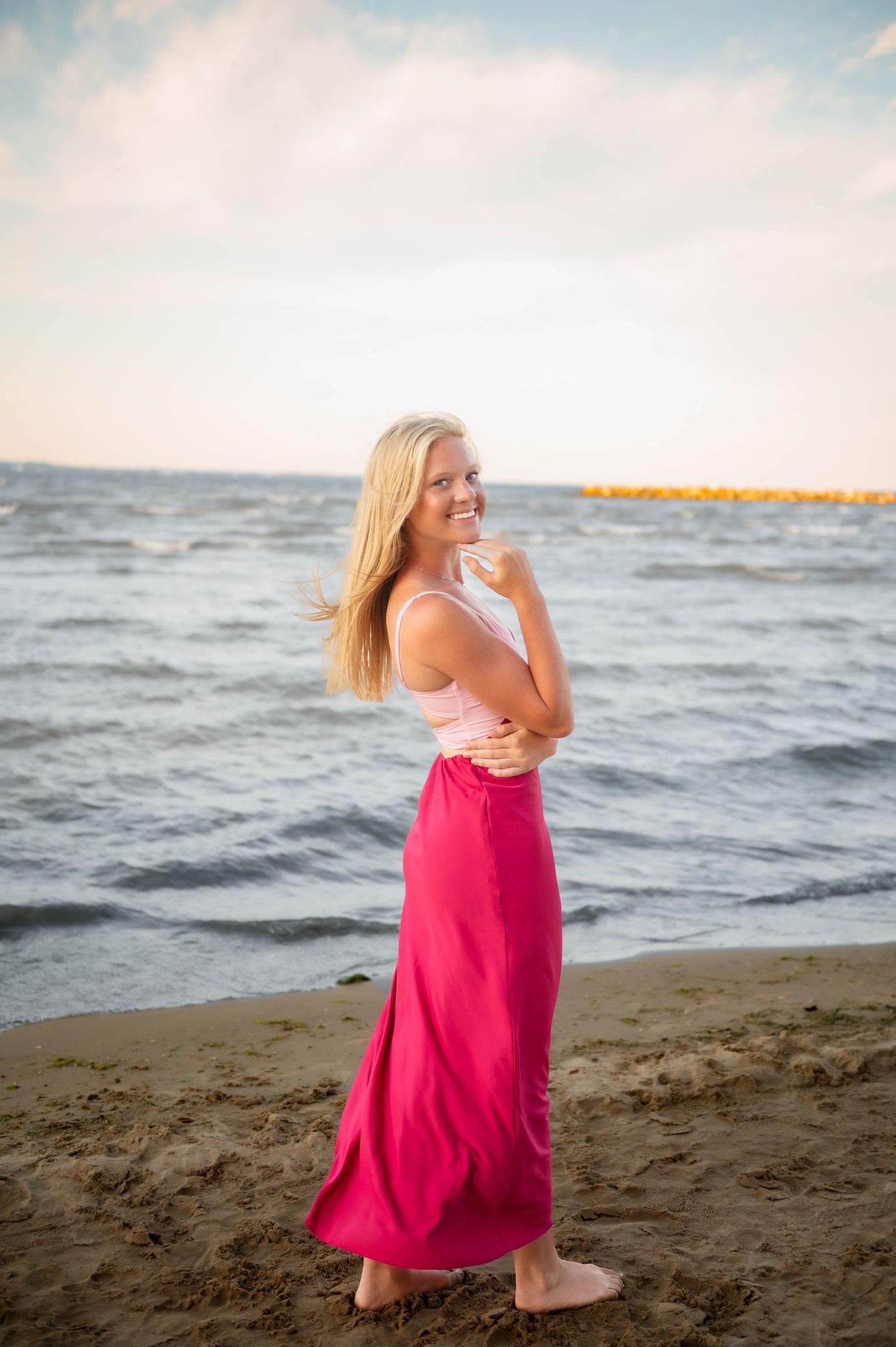 Woman in pink dress poses gracefully on beach at sunset.