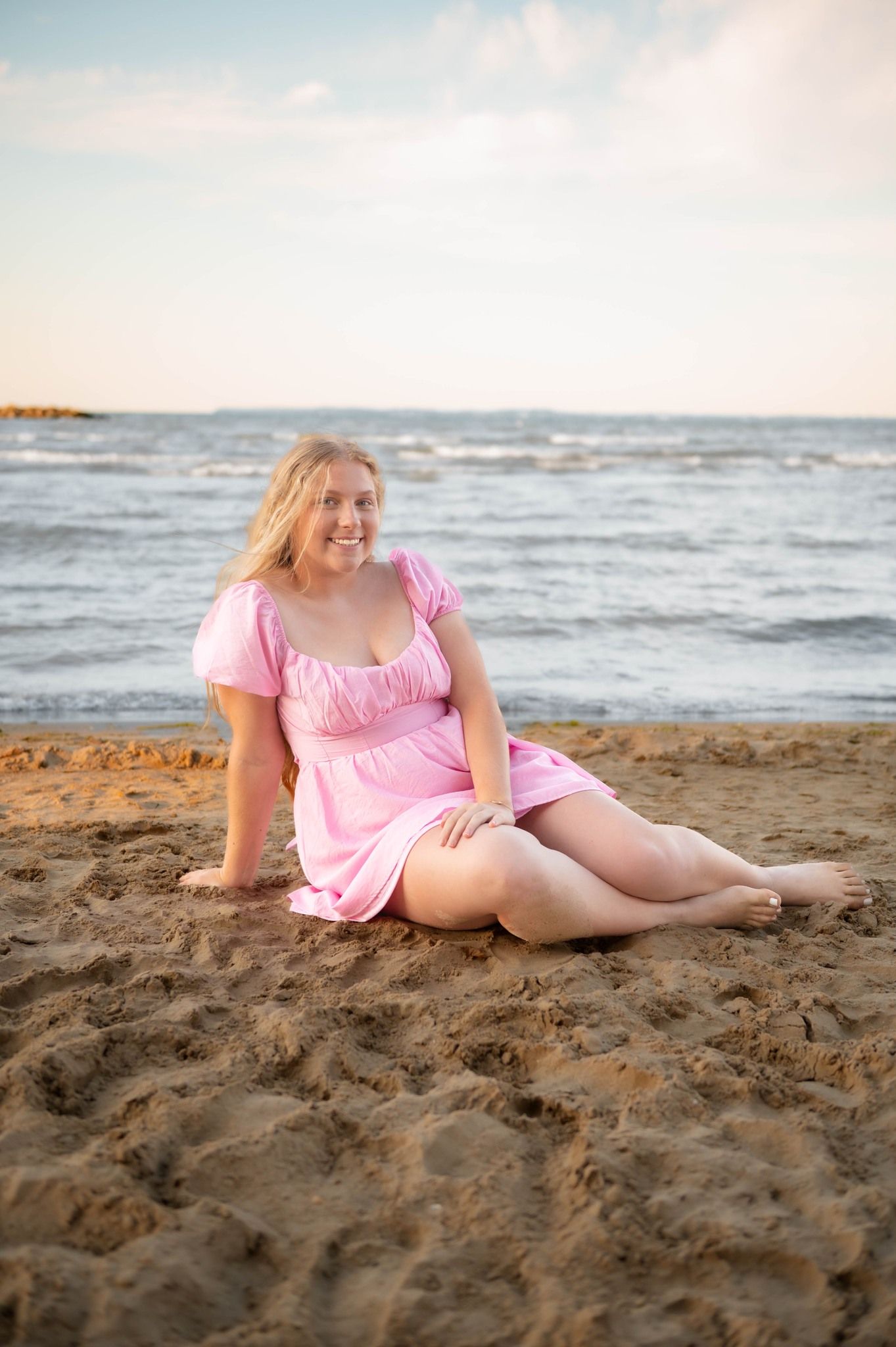 Person relaxing on sandy beach wearing pink summer dress.