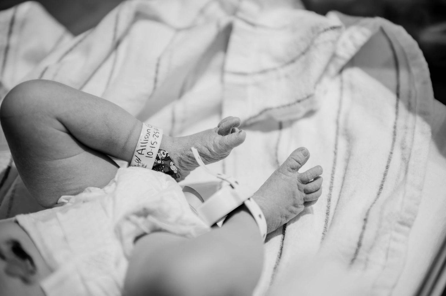 A newborn infant sleeps peacefully in a hospital bed with medical monitoring equipment.