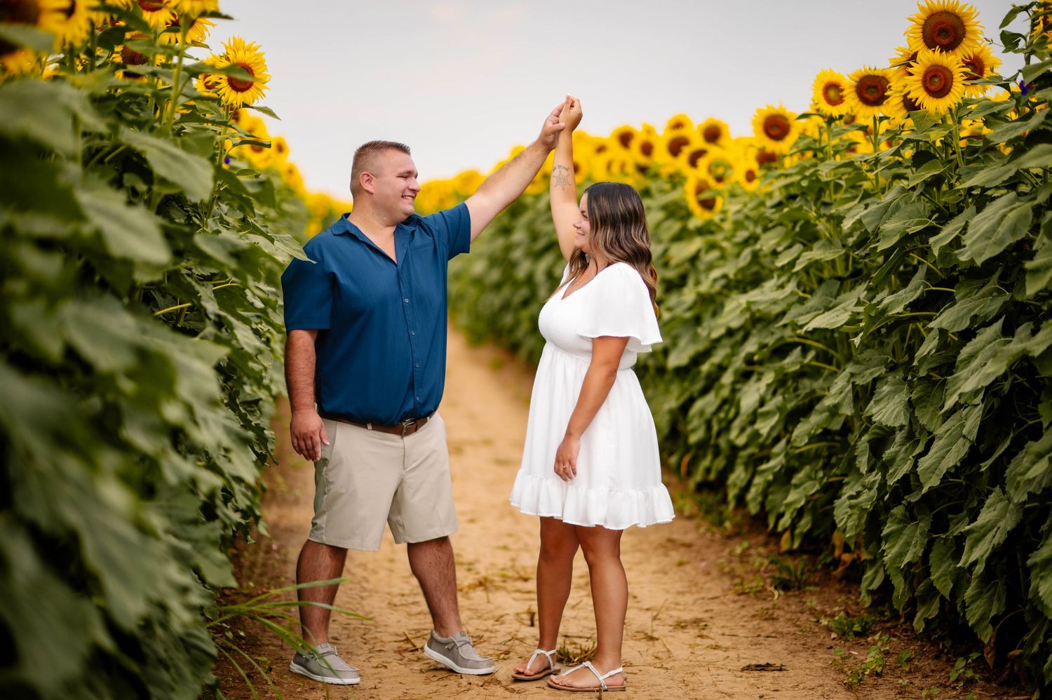 A couple sharing a playful high-five moment between rows of towering sunflowers.