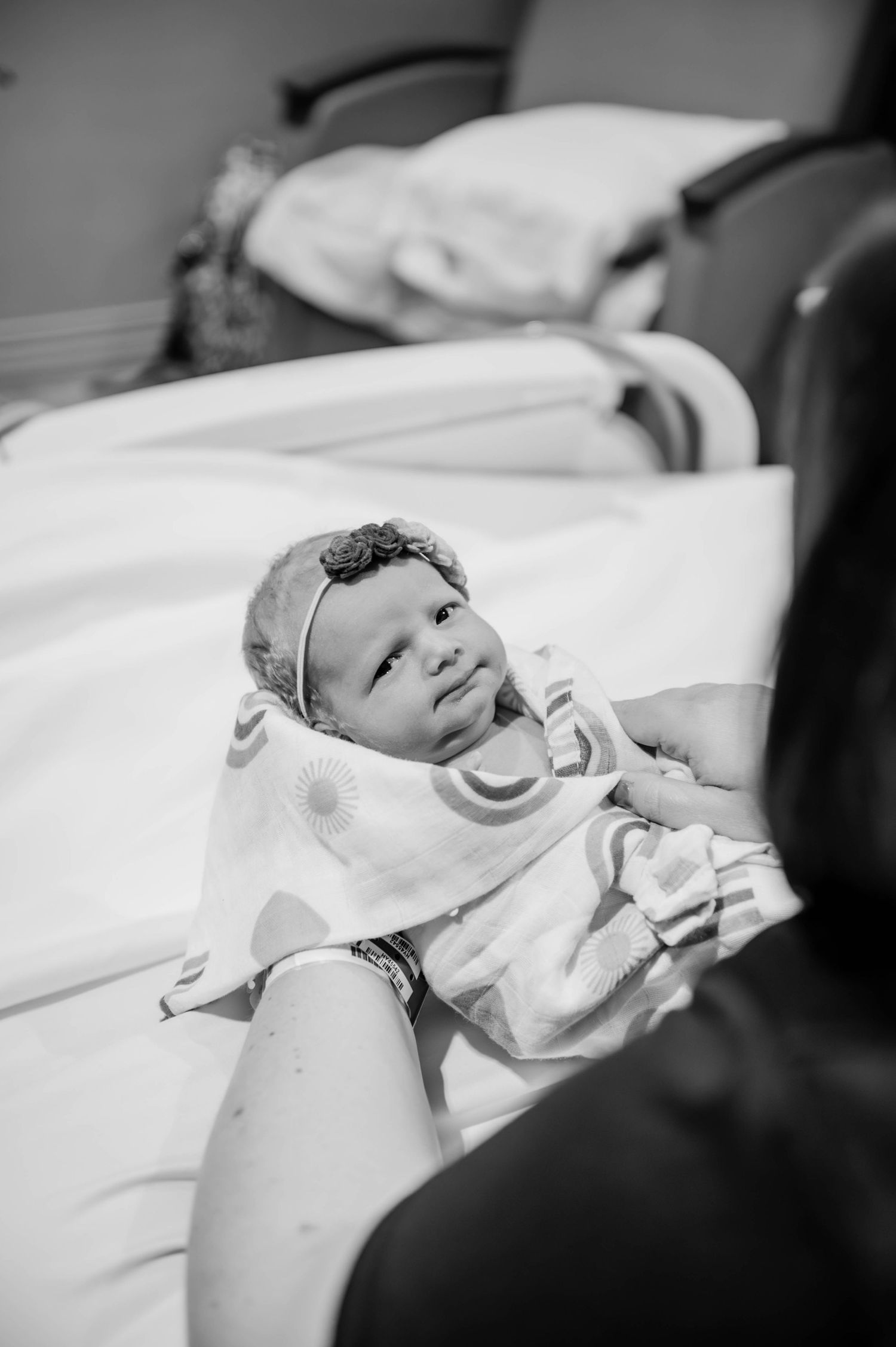 Sweet newborn baby wearing a headband rests peacefully in their hospital bed.