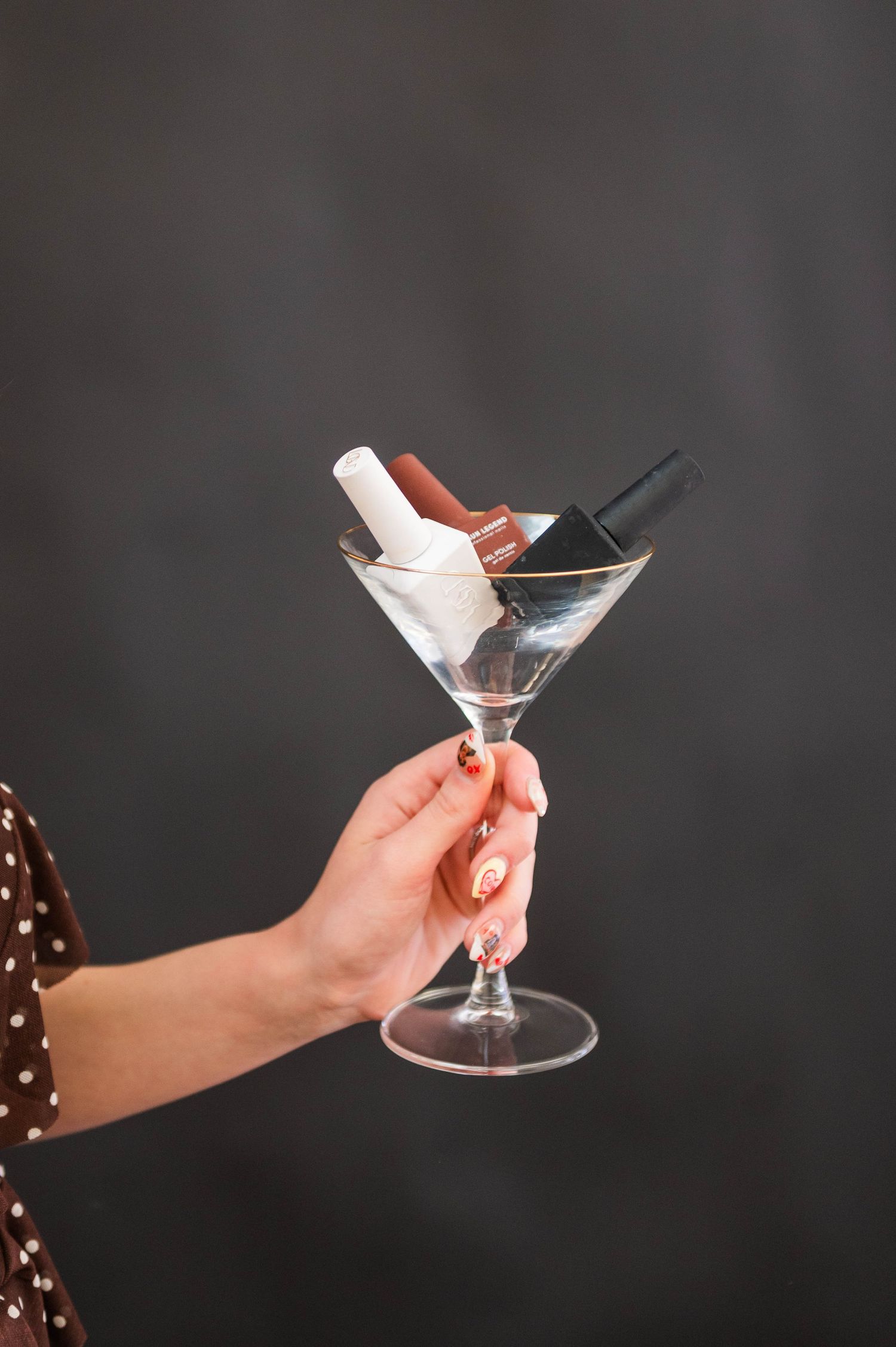 Hands hold martini glasses against a dark background in an artistic composition.