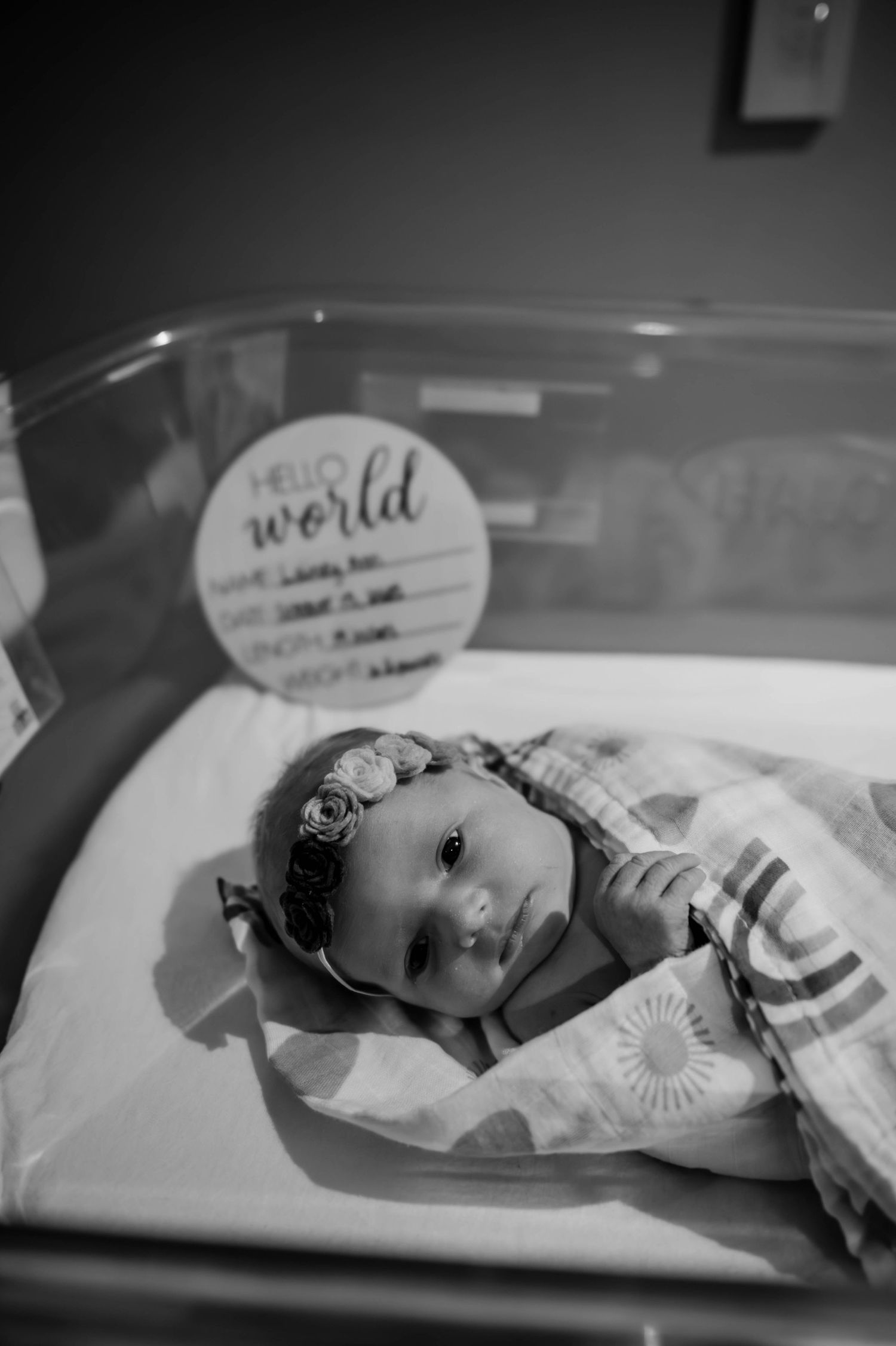 Newborn baby resting in a hospital bassinet with identification tags visible.
