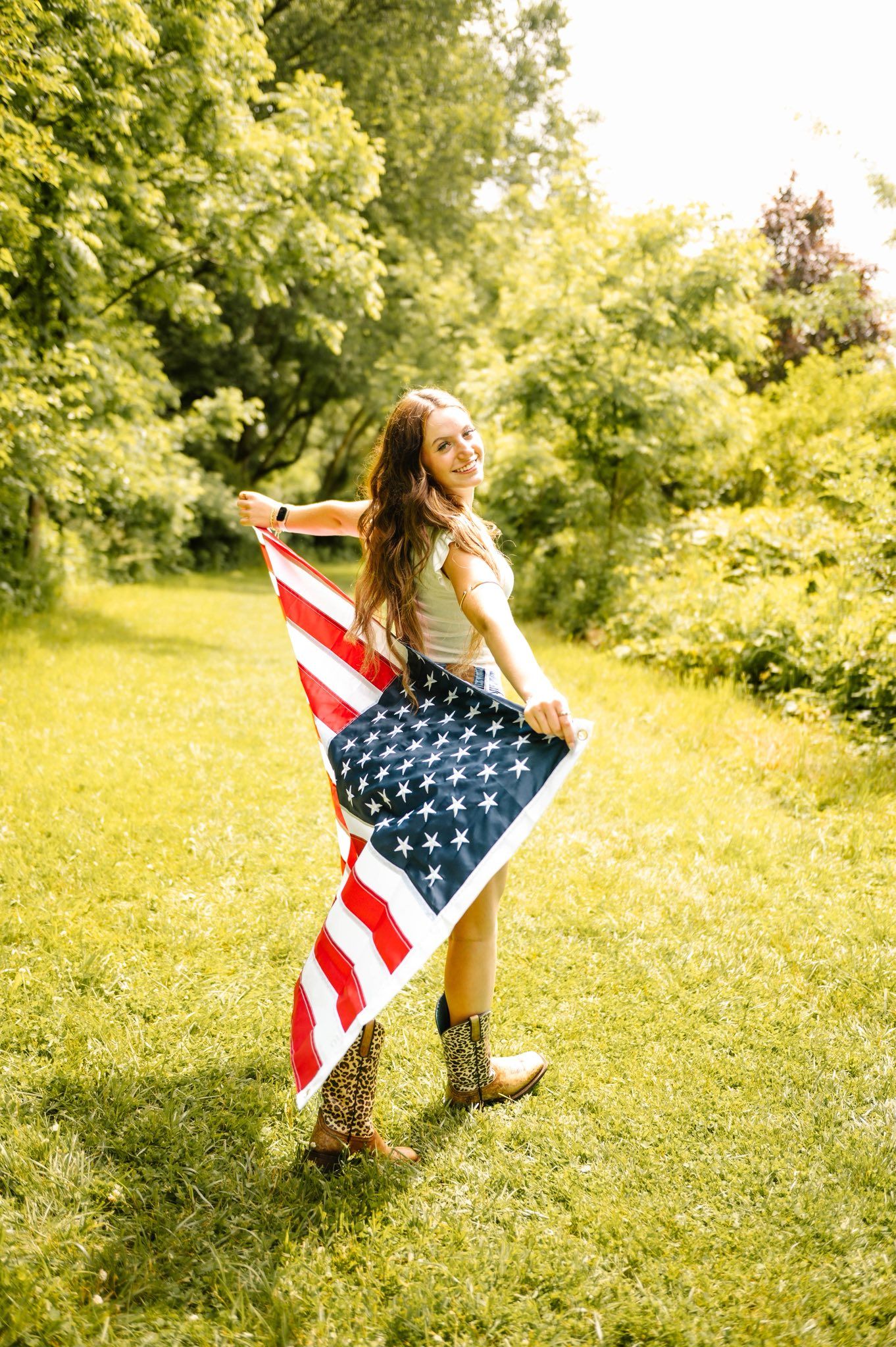 Person dances with American flag in sunlit meadow wearing casual attire.