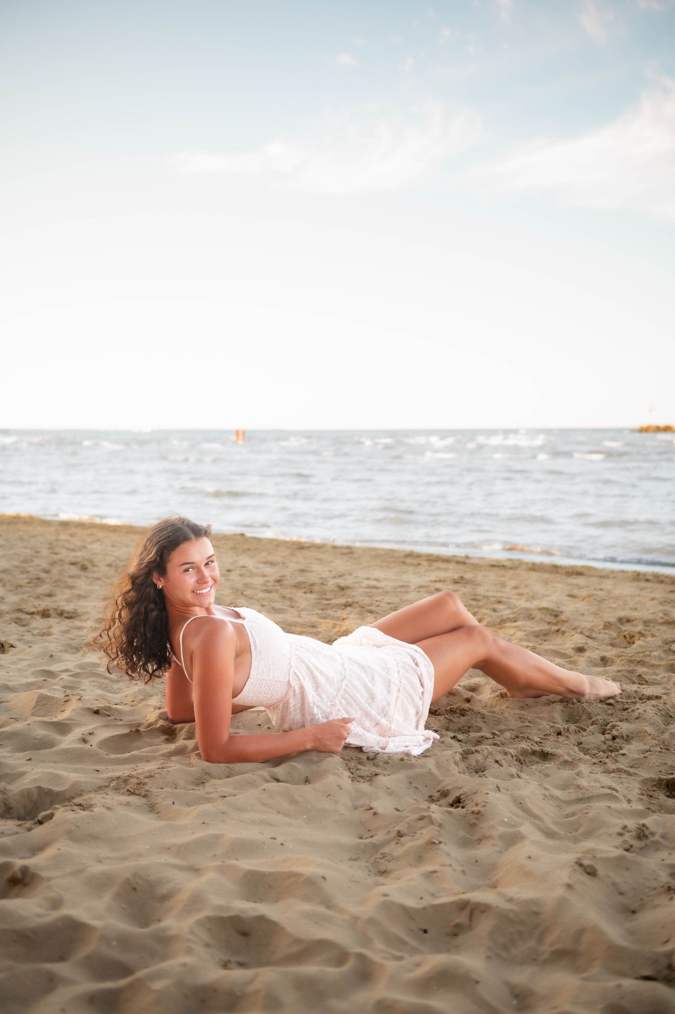 Woman in white sundress posing playfully on sandy beach at golden hour.