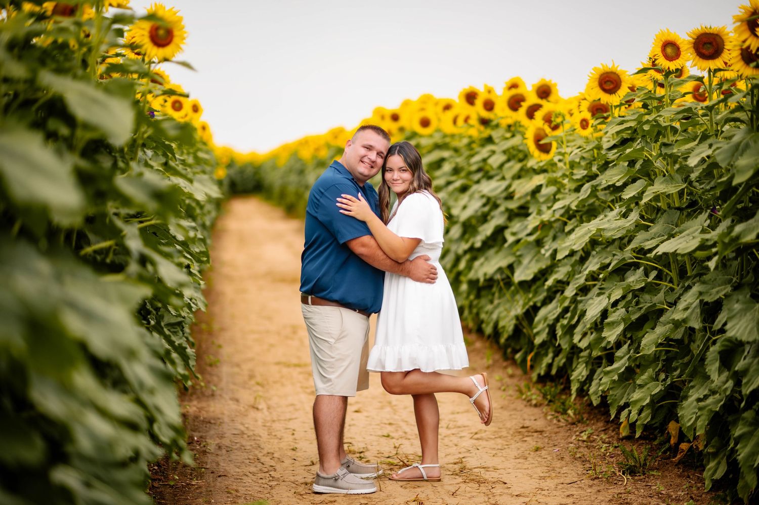 A romantic photoshoot among tall sunflowers with a couple walking down a dirt path.