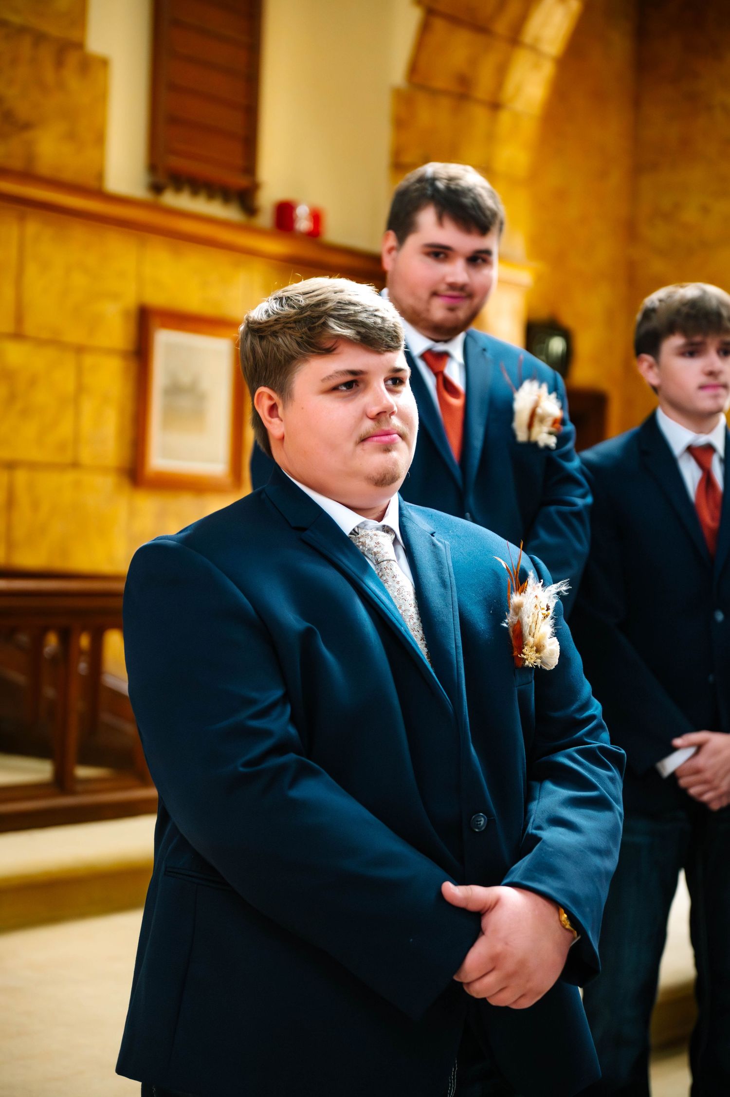 Groomsmen in dark suits stand in a formal indoor setting with warm lighting.
