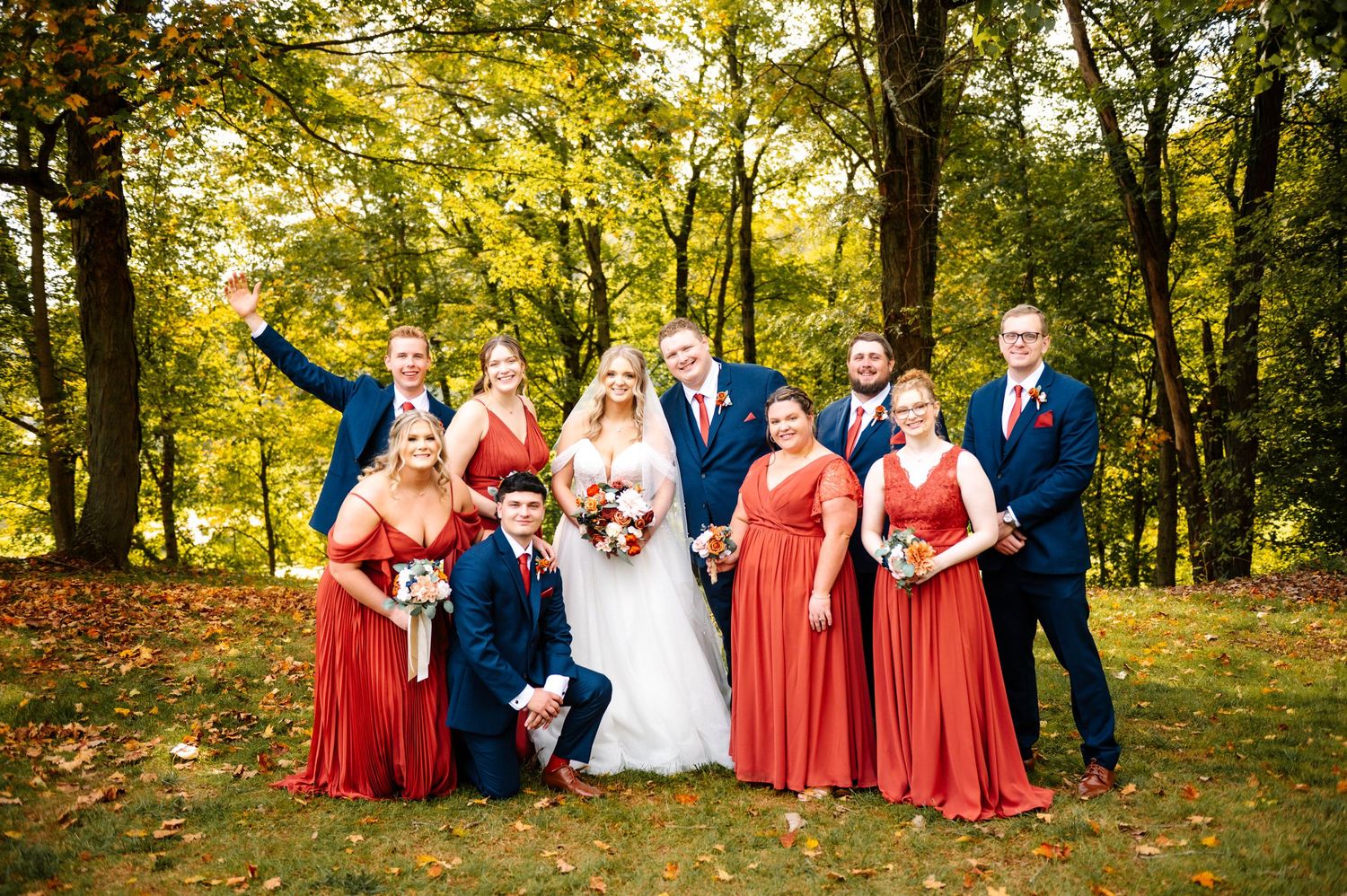 Wedding party in red and navy poses outdoors against autumn trees.