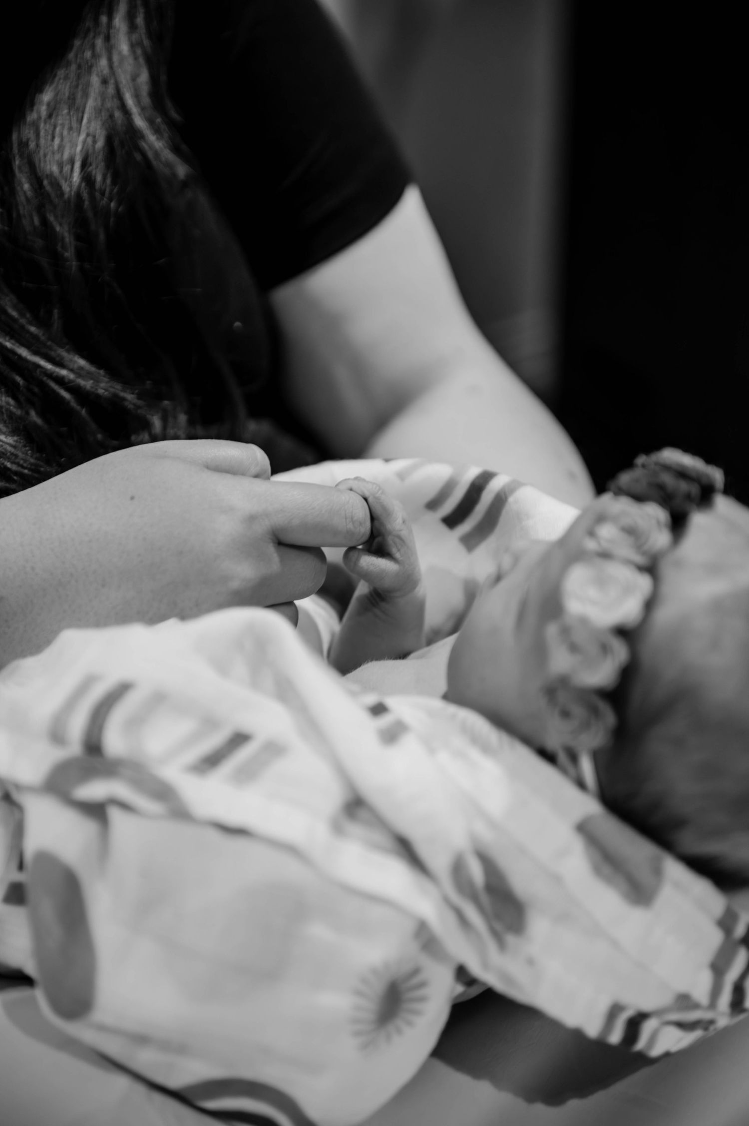 Intimate black and white image of a parent holding their newborn's tiny hand in the hospital.