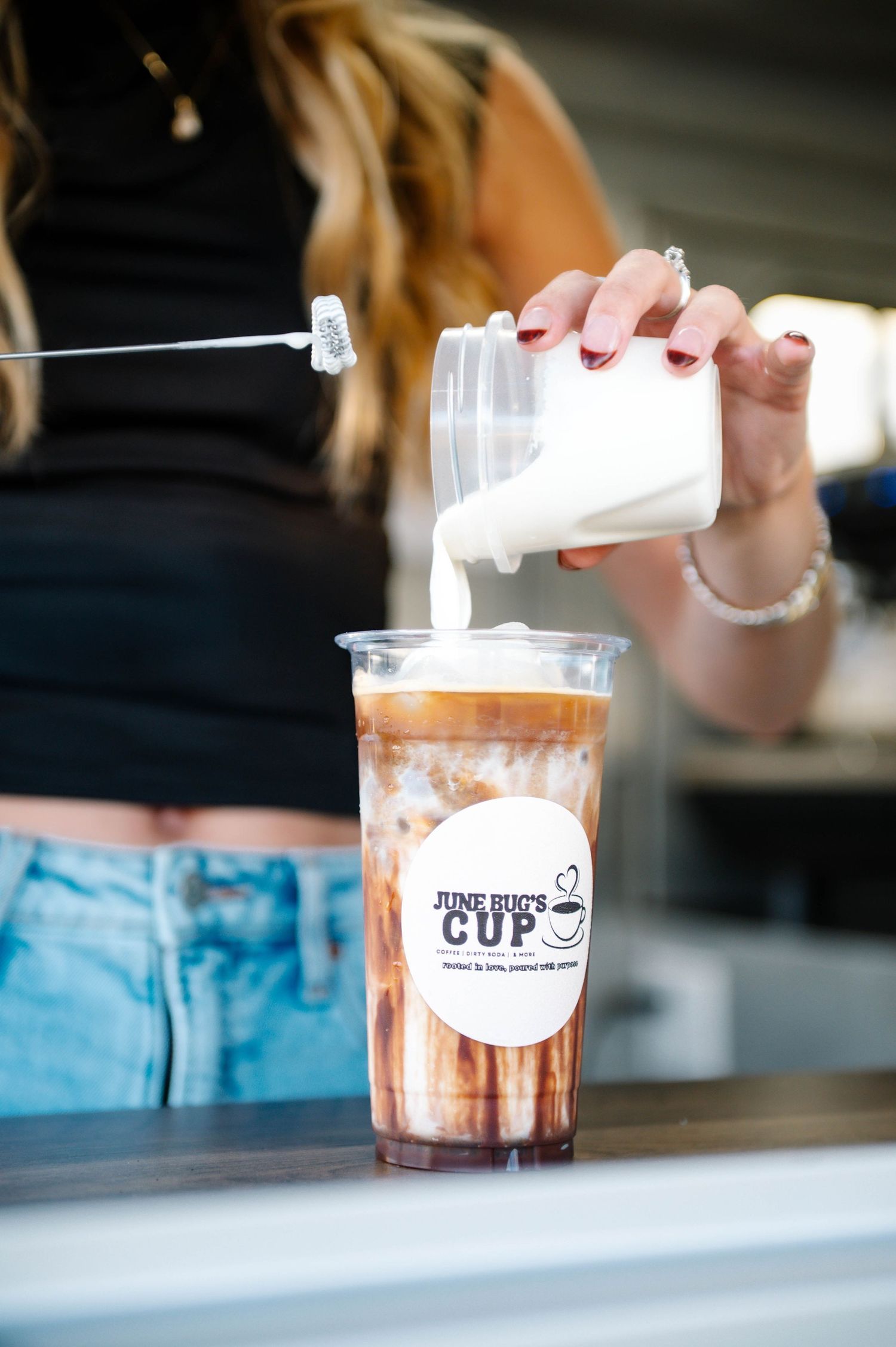 Preparing a cold drink in a branded plastic cup at a coffee shop counter.