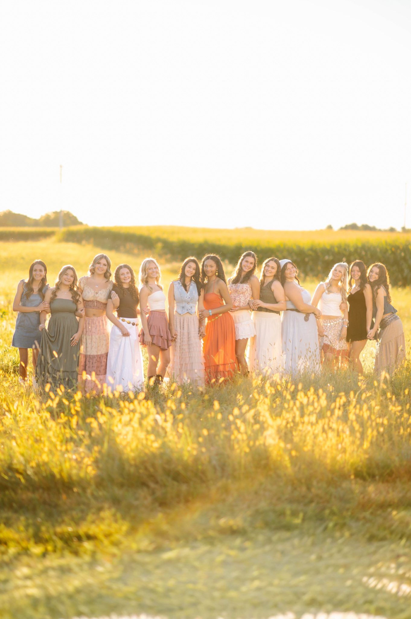 Group portrait in flowing dresses against golden sunset field.