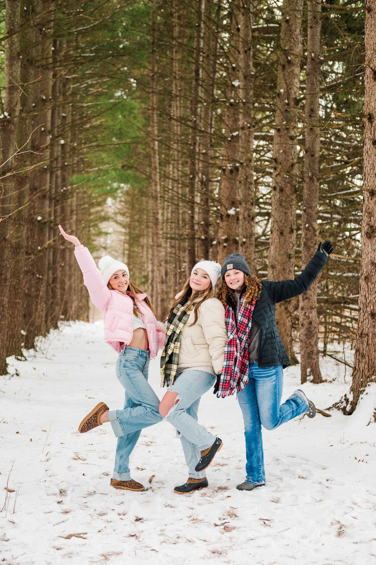 Group of friends jump and pose playfully in the snow surrounded by tall pine trees.