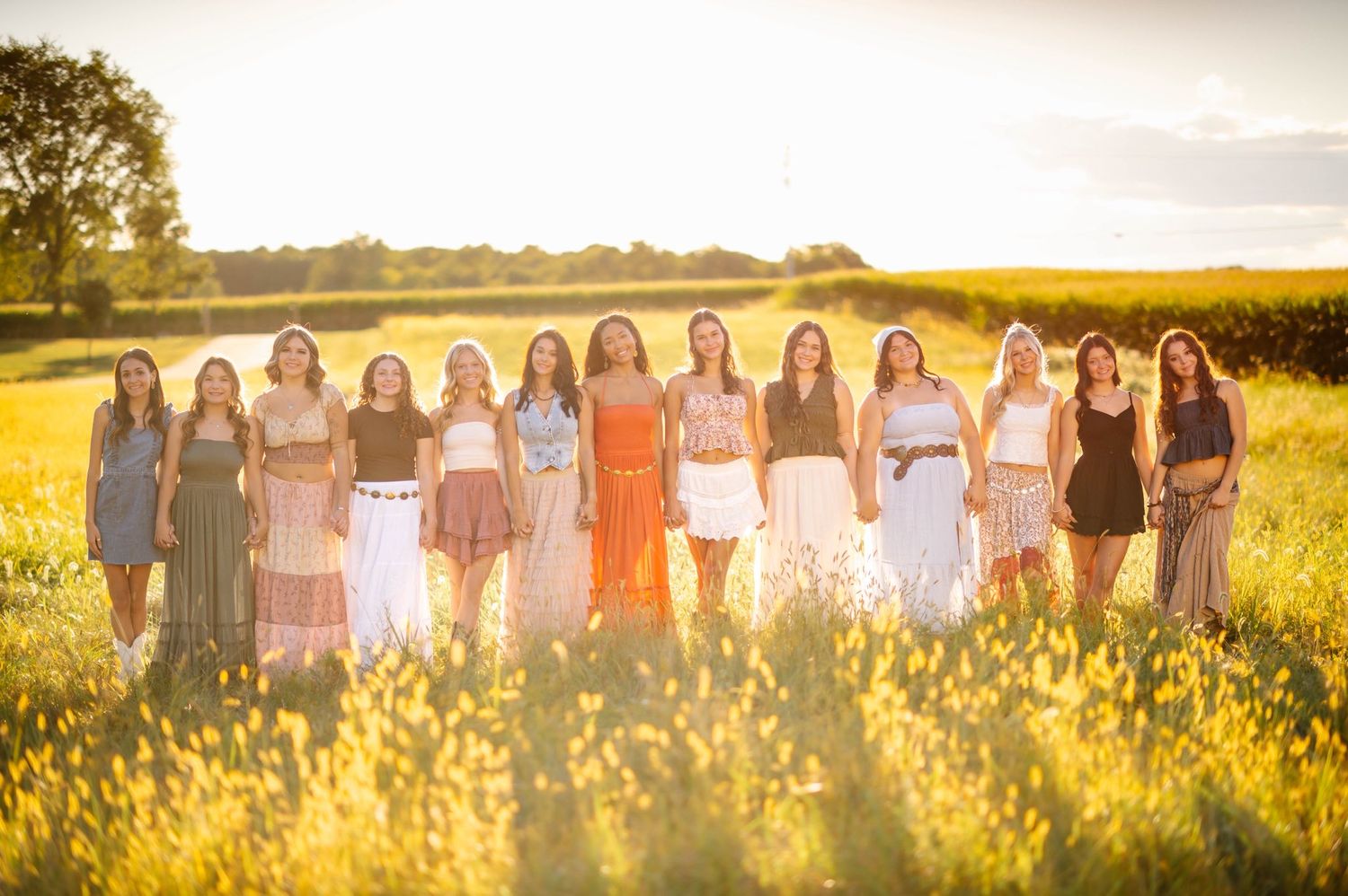 Row of friends in summer attire posing in a golden meadow at dusk.