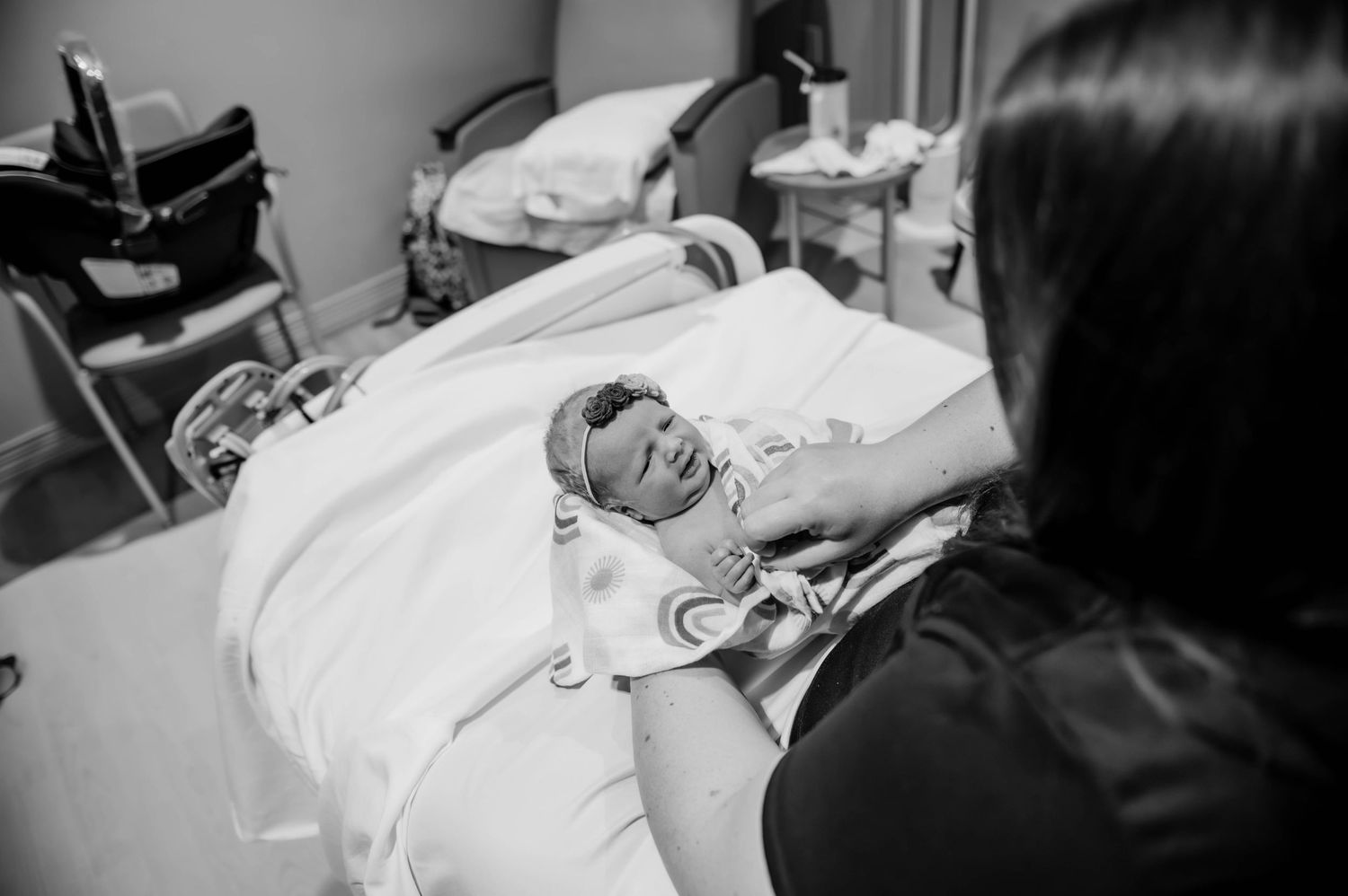 Black and white image of a newborn infant lying in a hospital bassinet while being cared for.