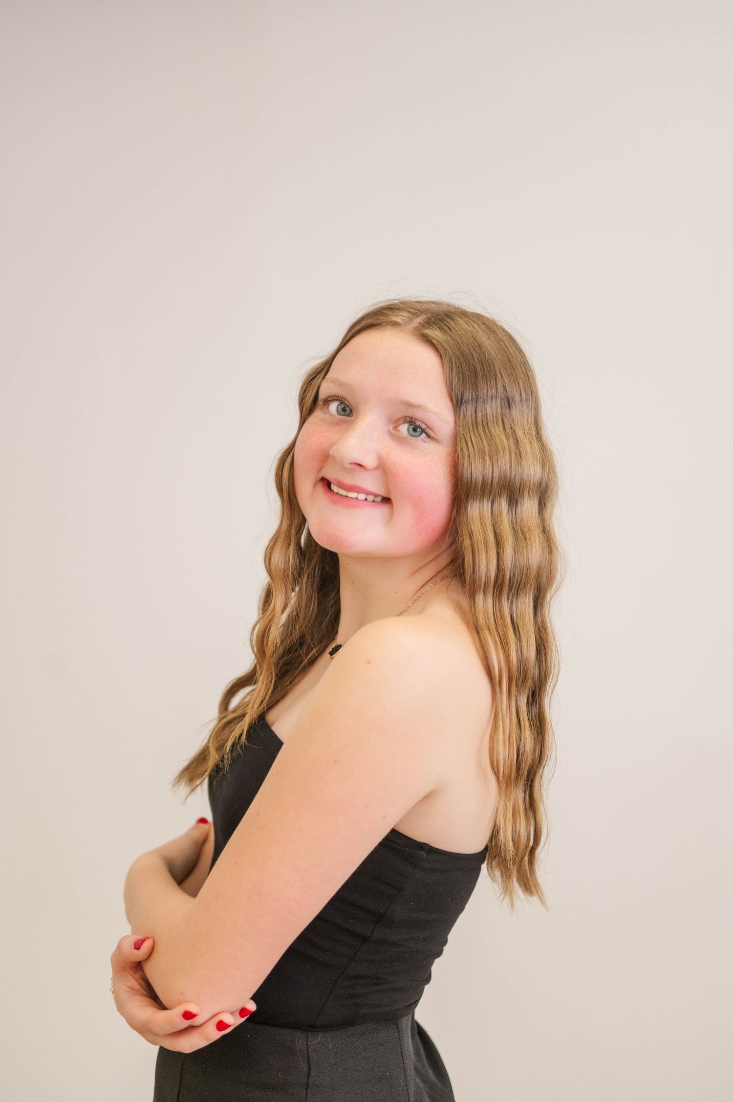 Smiling young girl with wavy hair in a black strapless top posing with arms crossed.