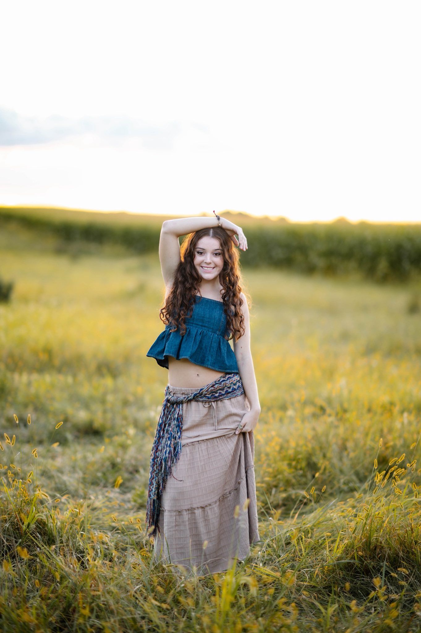 Person in blue top and tan skirt posing in sunny wildflower field.