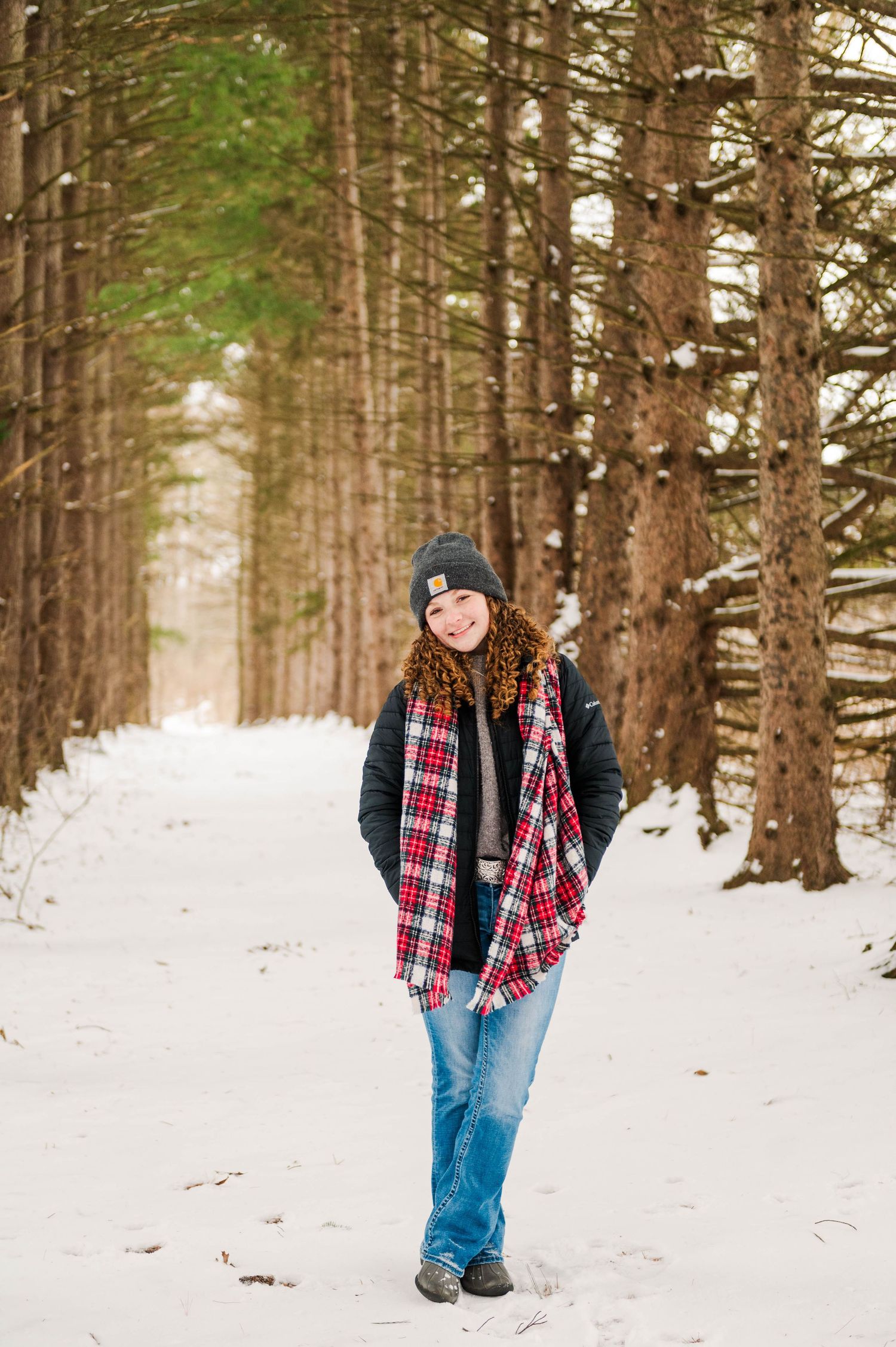 Winter portrait session featuring plaid and denim against a snowy forest backdrop.