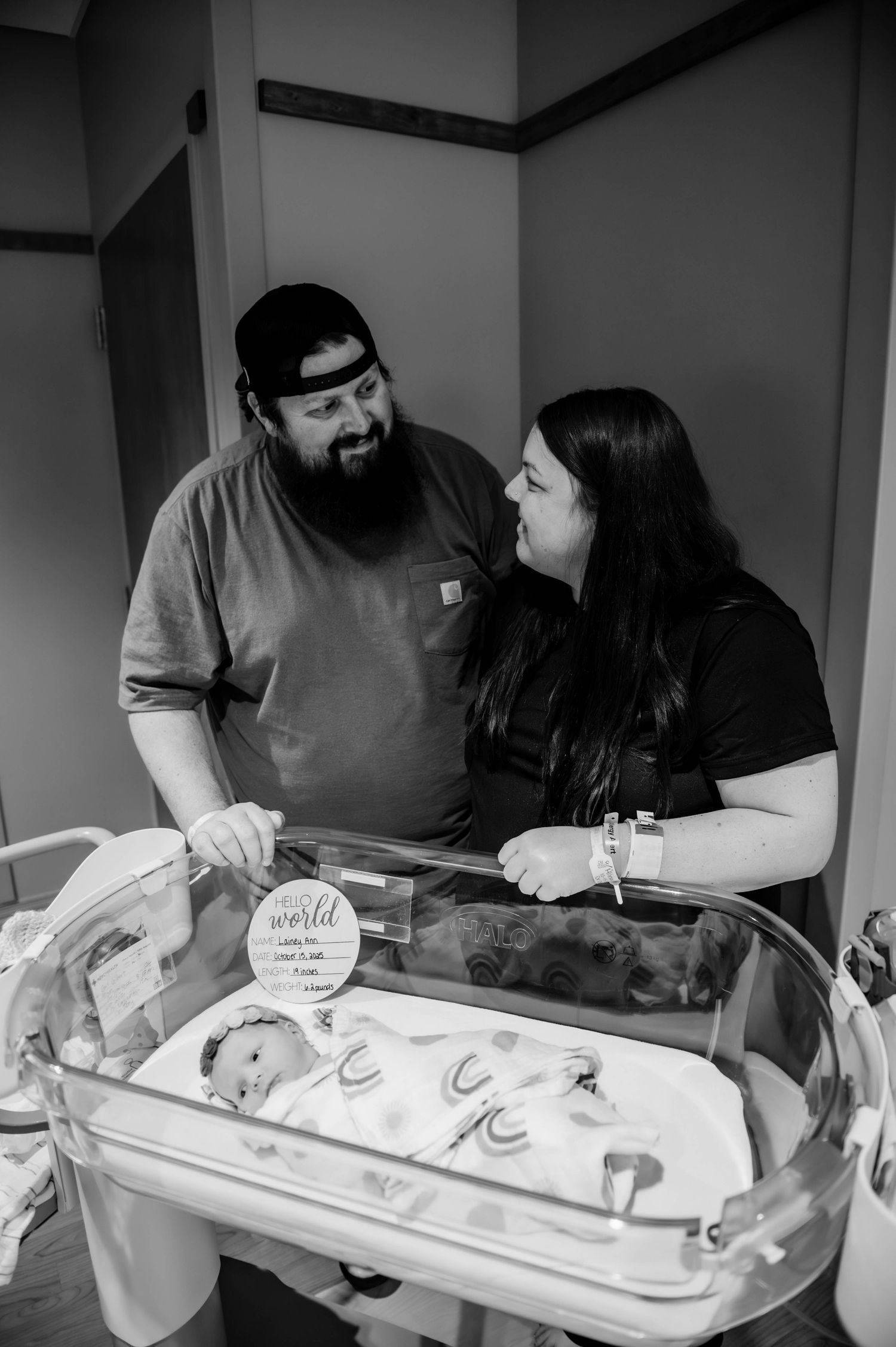 Parents lean over a hospital bassinet to admire their newborn in a tender moment.