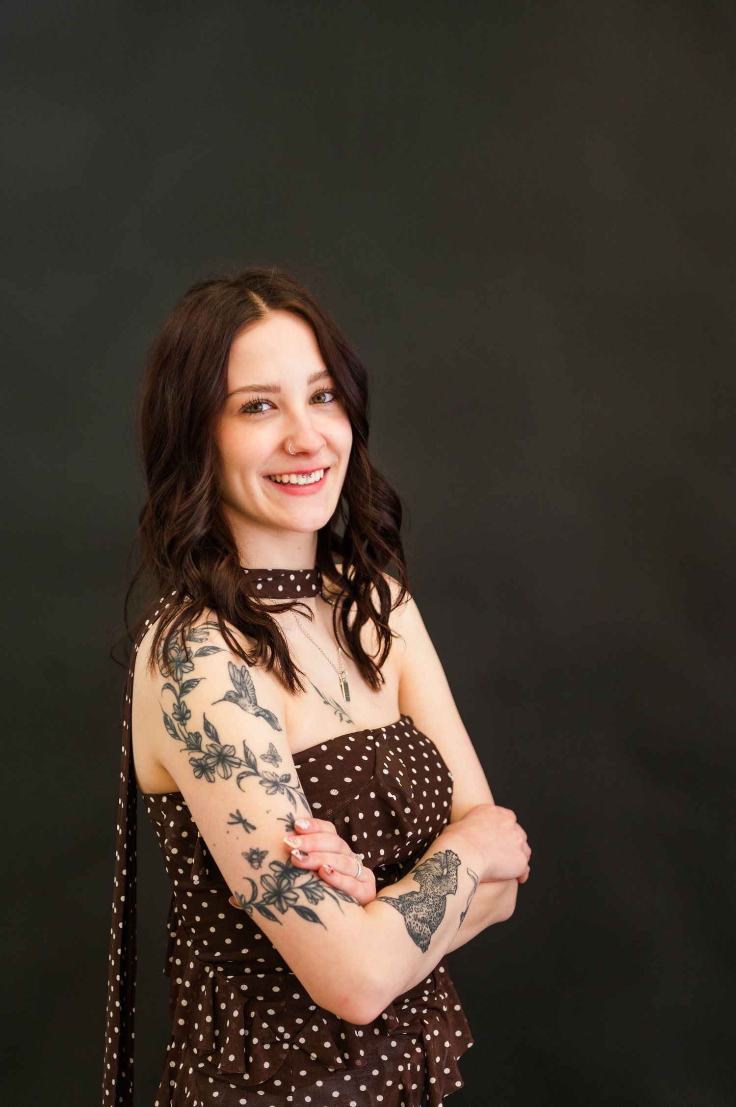 Studio portrait with polka dot dress and tattoos against dark background.