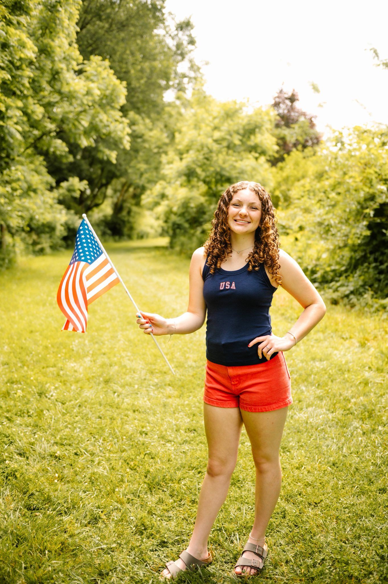 A patriotic summer photoshoot with American flags in a grassy field.